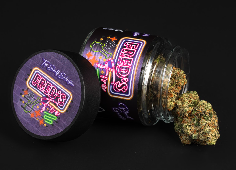 A jar labeled 'Fred's Fire' with cannabis buds spilling out onto a black surface.