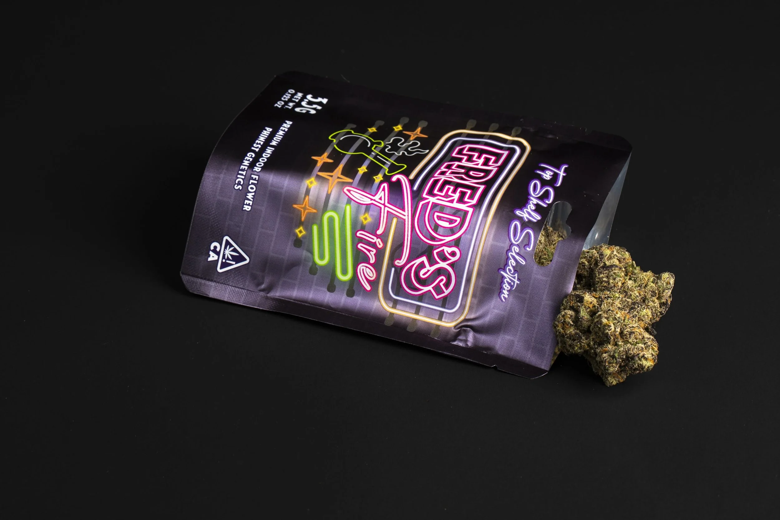 Purple bag of cannabis labeled 'Fried Sours' with a cannabis bud next to it on a black surface.