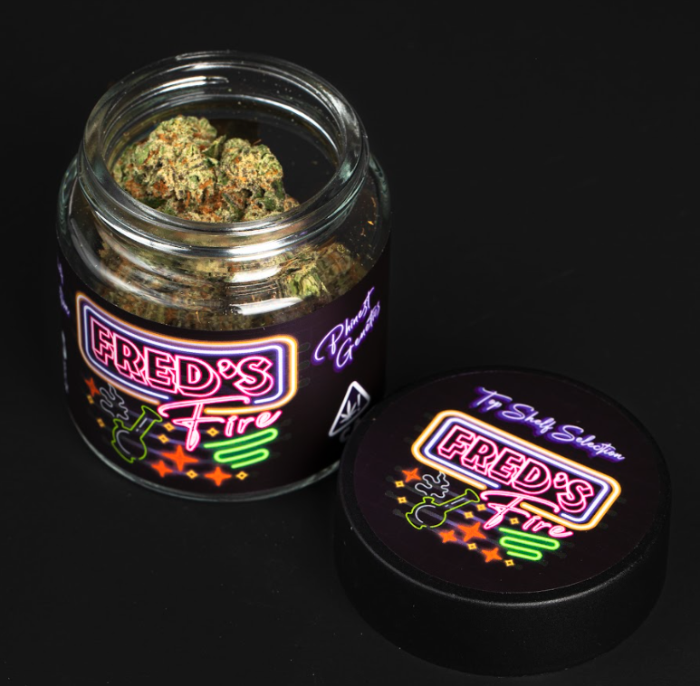 A glass jar with a neon-style label reading 'Fred's Fire' and containing cannabis buds, alongside a black cap with the same neon labe.