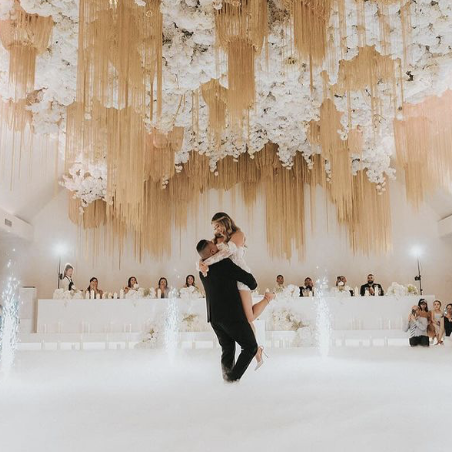 Couple dancing at a wedding reception with floral and fabric decorations overhead.