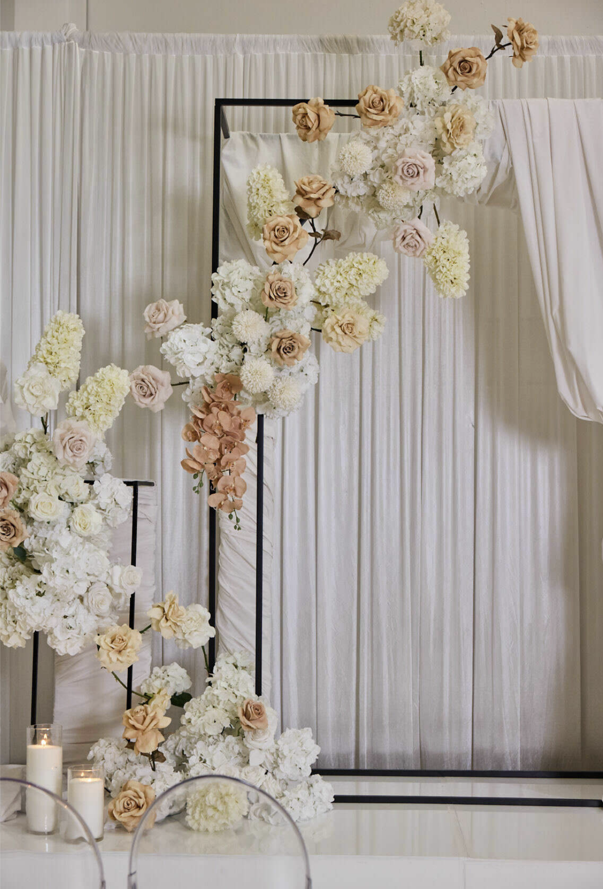 Floral wedding arch with white, cream, and blush roses, hydrangeas, and orchids against cream-colored draped fabric.