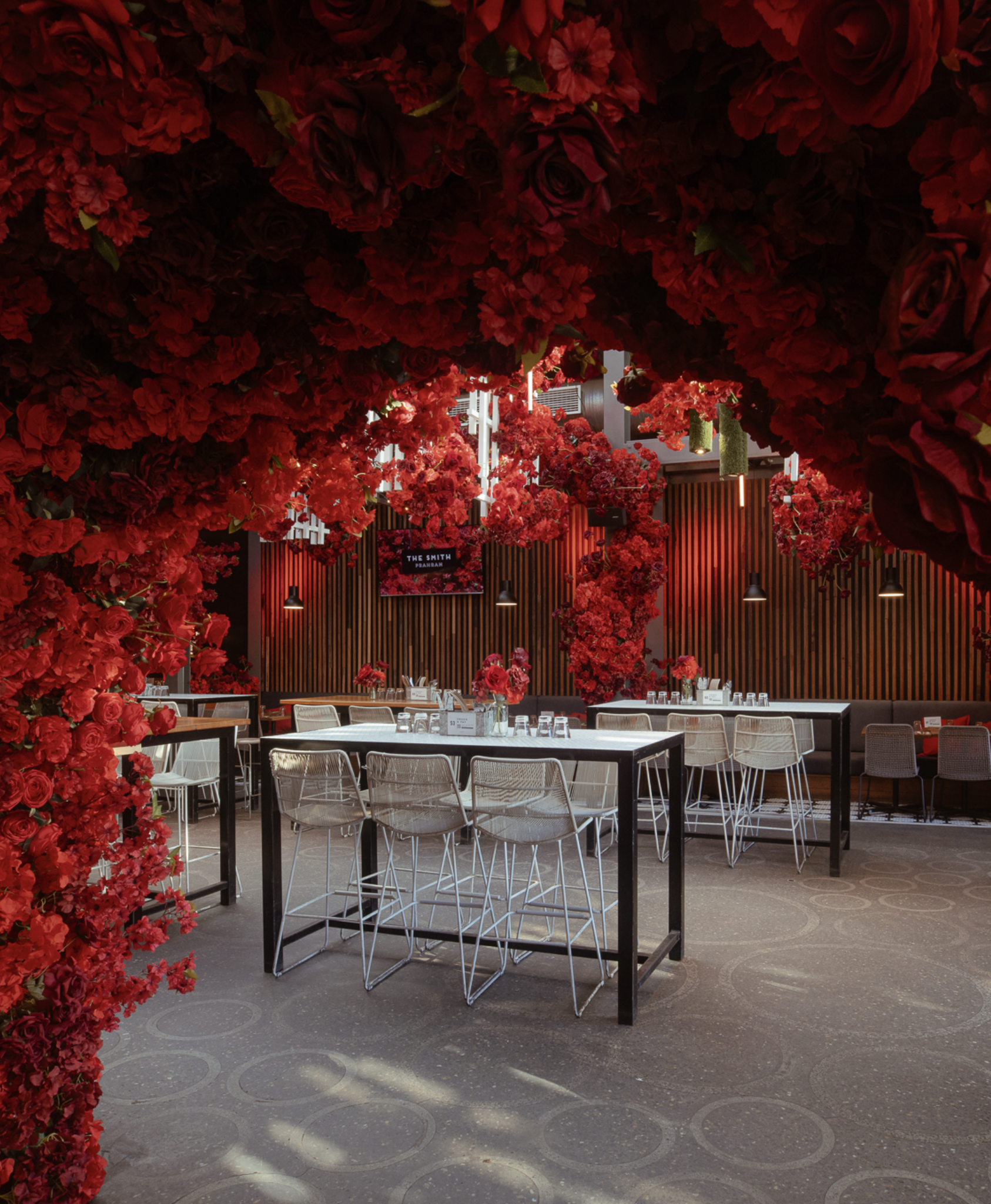 A restaurant interior decorated with red flowers and floral arrangements, with tables and chairs set for dining.