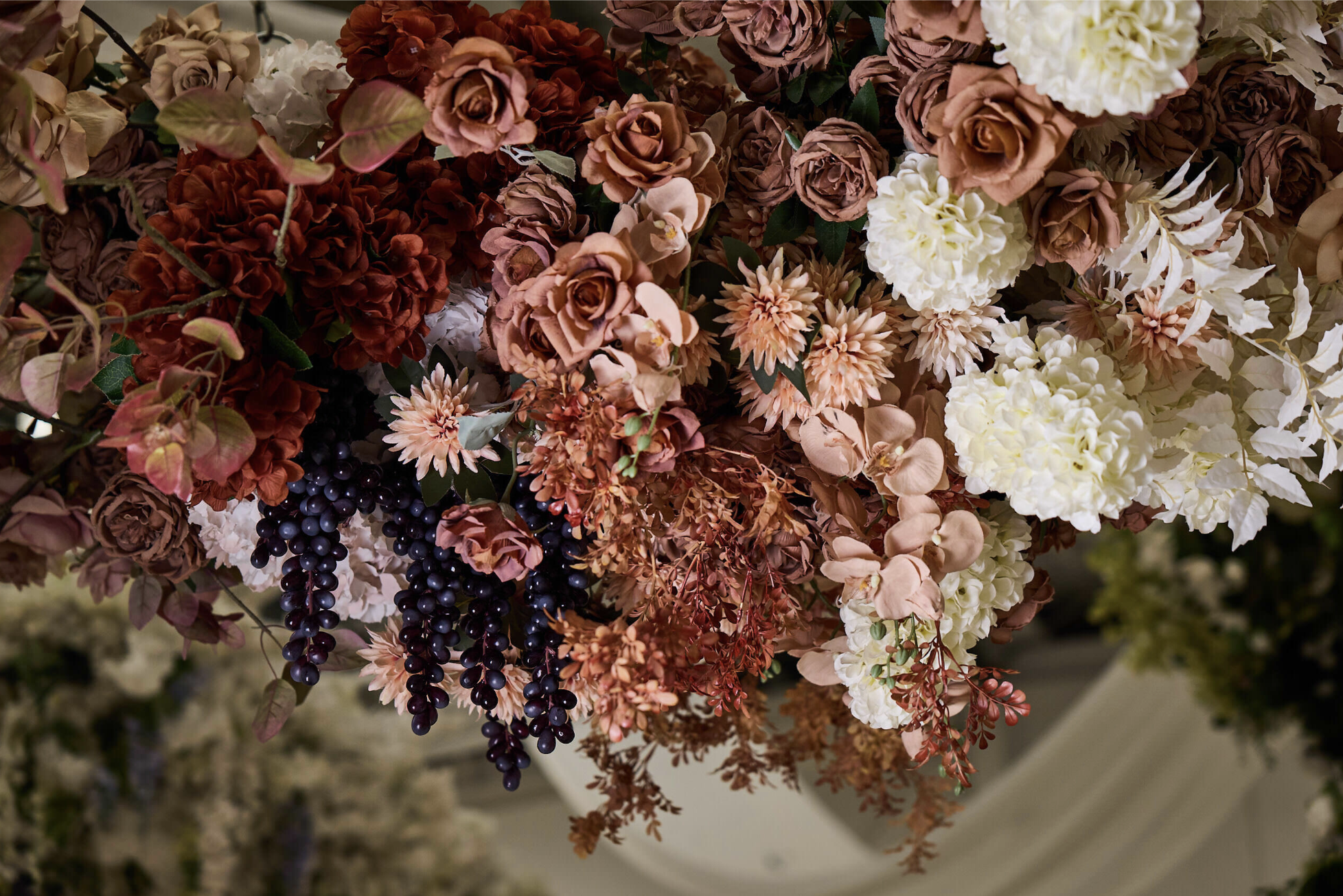 Close-up of a floral arrangement with roses, hydrangeas, dahlias, and hanging berries in shades of pink, white, and deep purple.