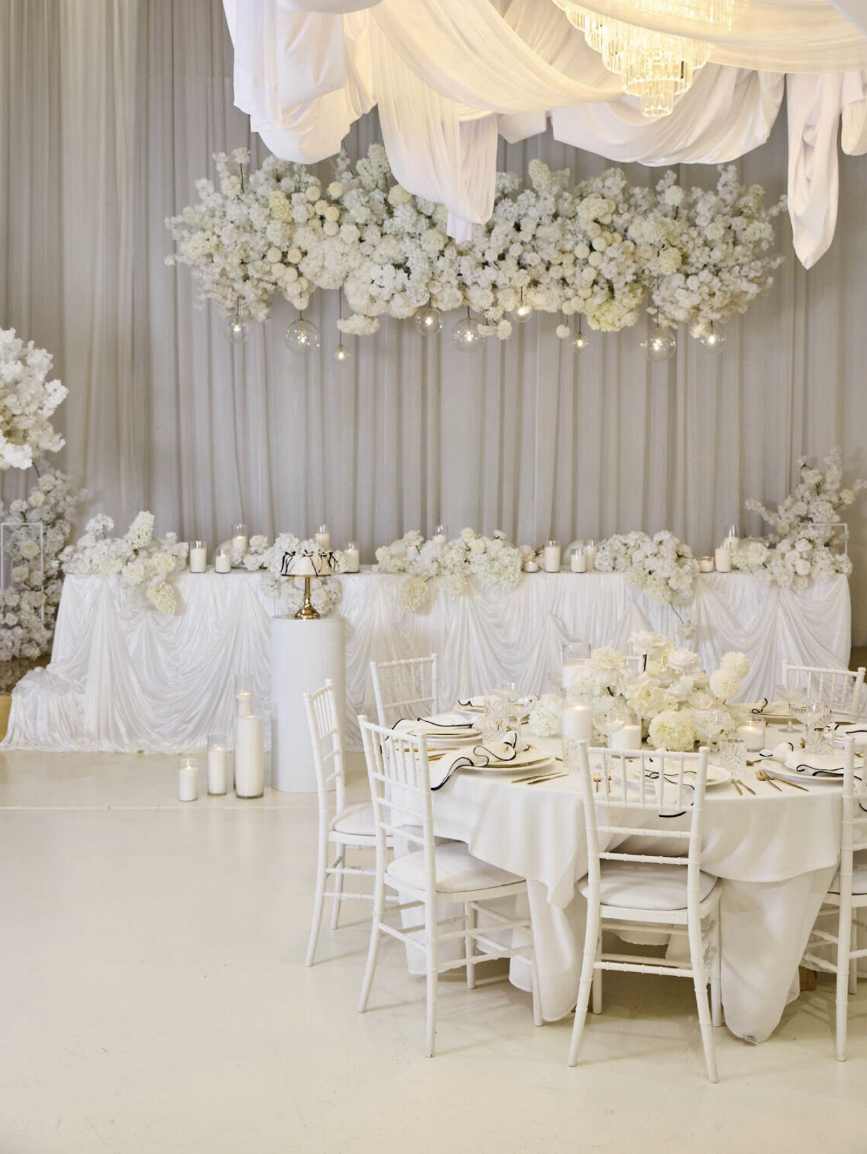 Elegant wedding reception decorated with white flowers, draped fabric, candles, and a chandeliers.
