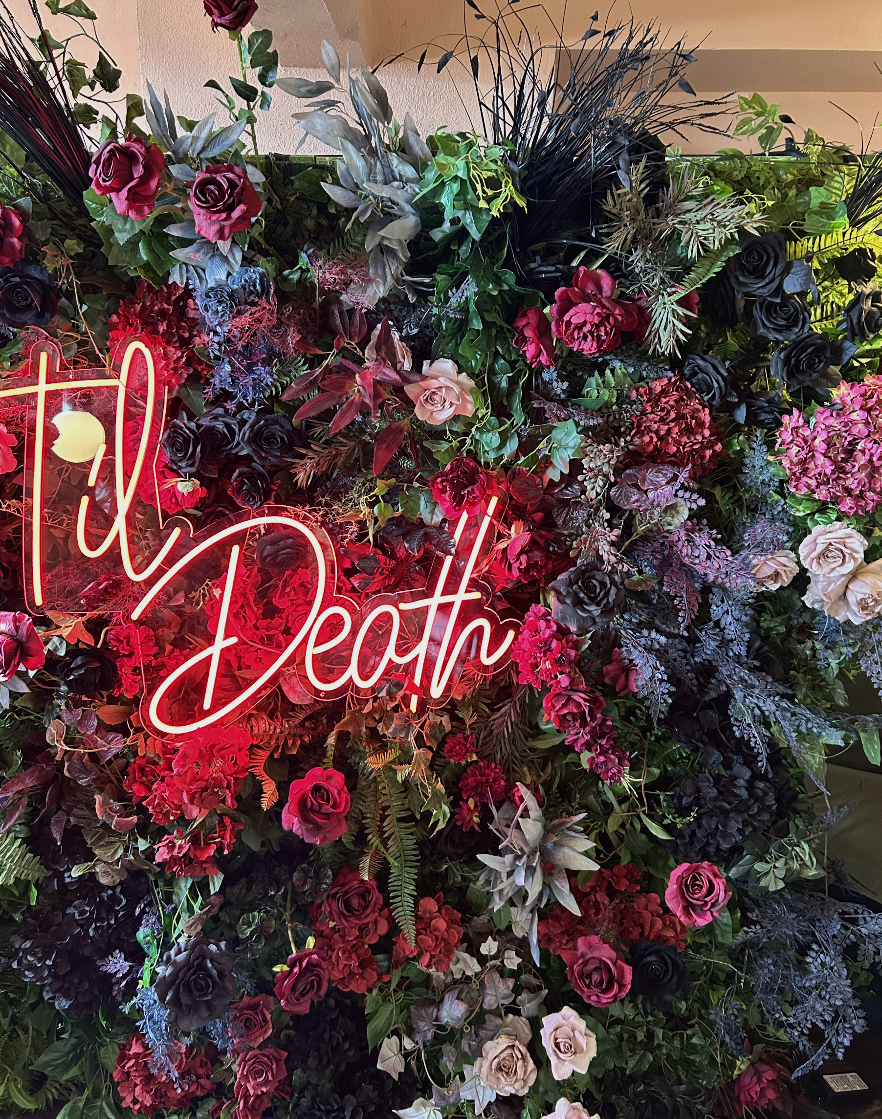 A floral arrangement with roses, hydrangeas, and foliage, featuring a neon sign that reads 'RIP Death' in red cursive lights.