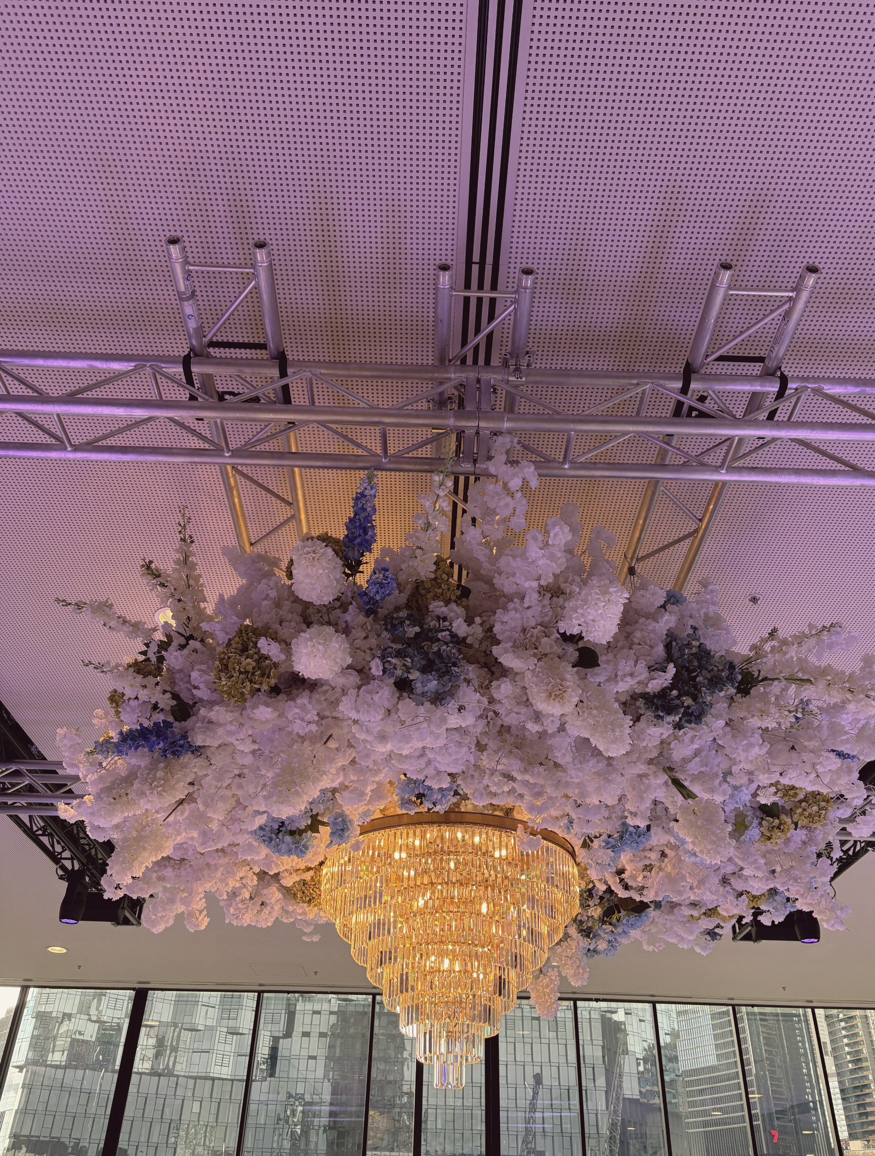 Elegant chandelier hanging from ceiling, surrounded by a floral arrangement of white, pink, and blue flowers.