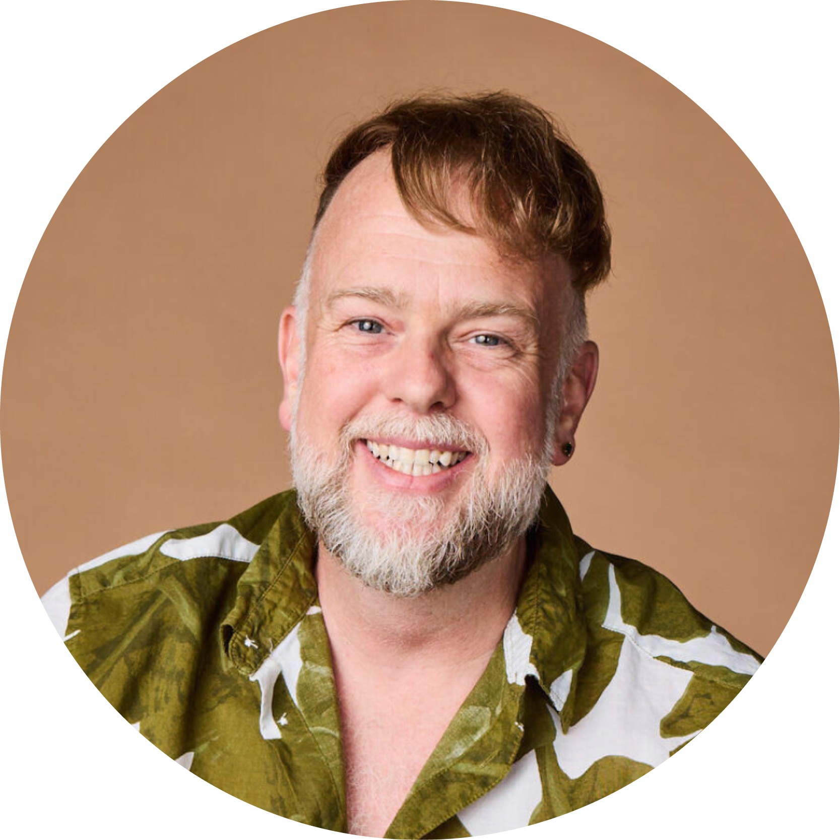 A smiling man with a beard and mustache, wearing a green and white patterned shirt, against a brown background.