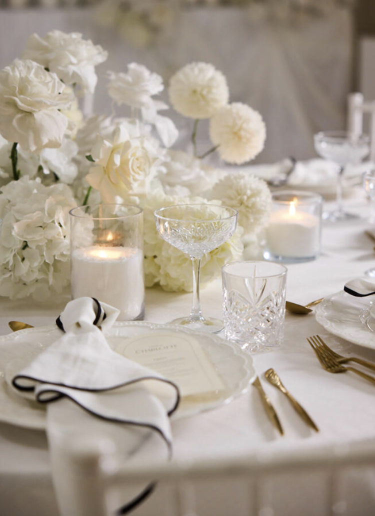 Elegant table setting with white flowers, candles, a menu, gold cutlery, and crystal glassware.