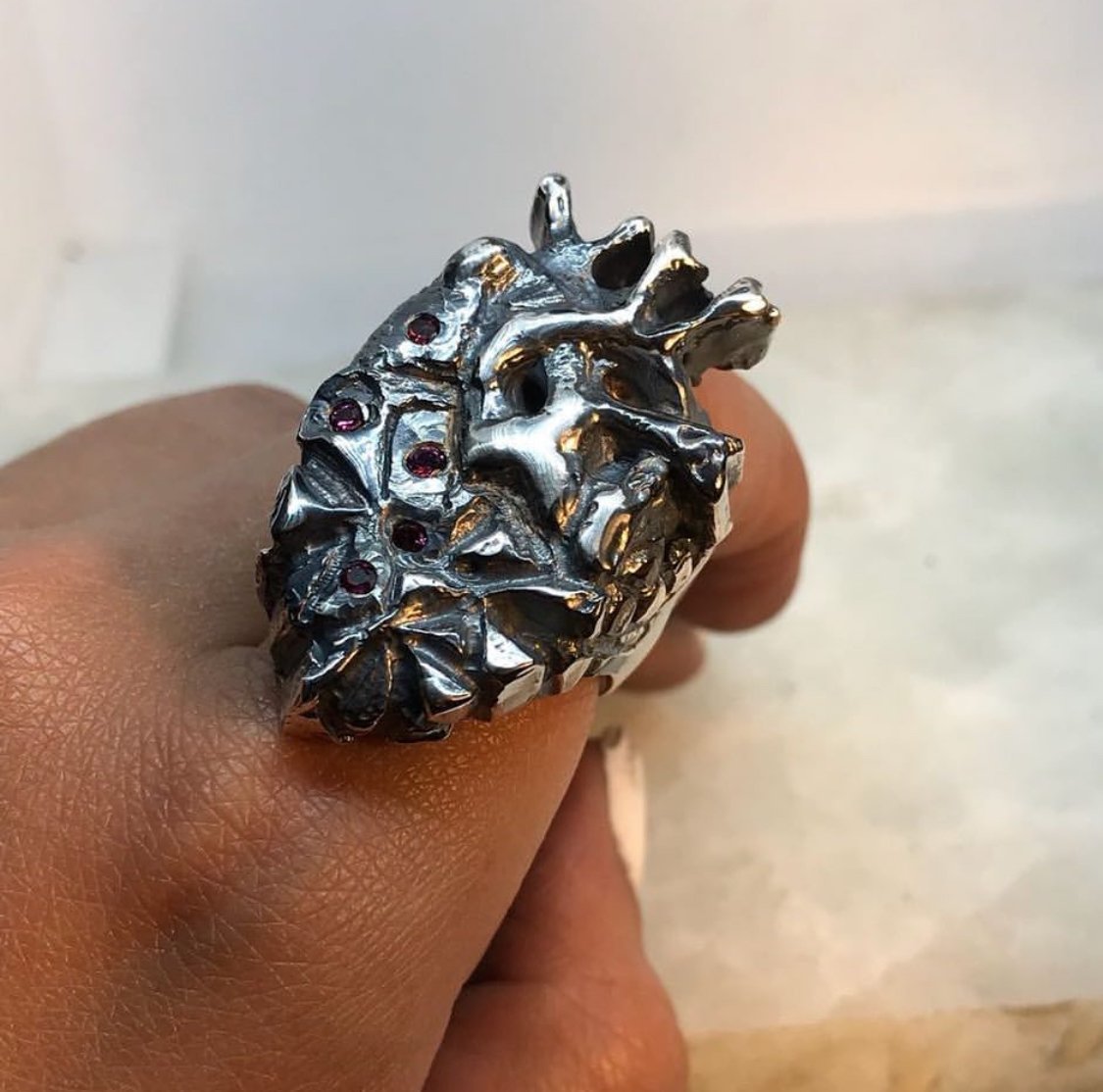 Anillo con forma de corazón anatómico, hecho de plata y con granates incrustados.