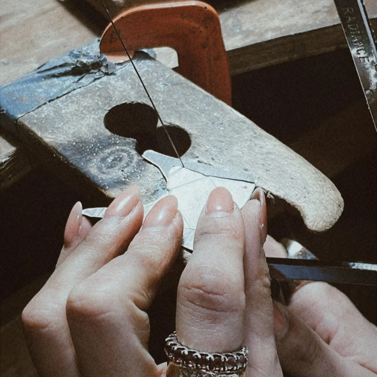 Mano sosteniendo una pieza de metal que se está cortando en un taller de joyería