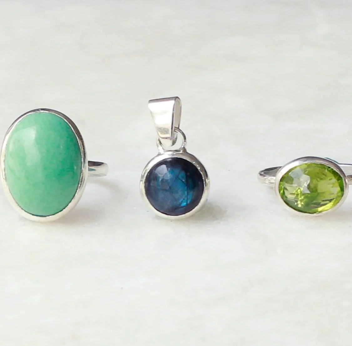 Tres anillos y un colgante con piedras color verde, azul y verde, en plata.