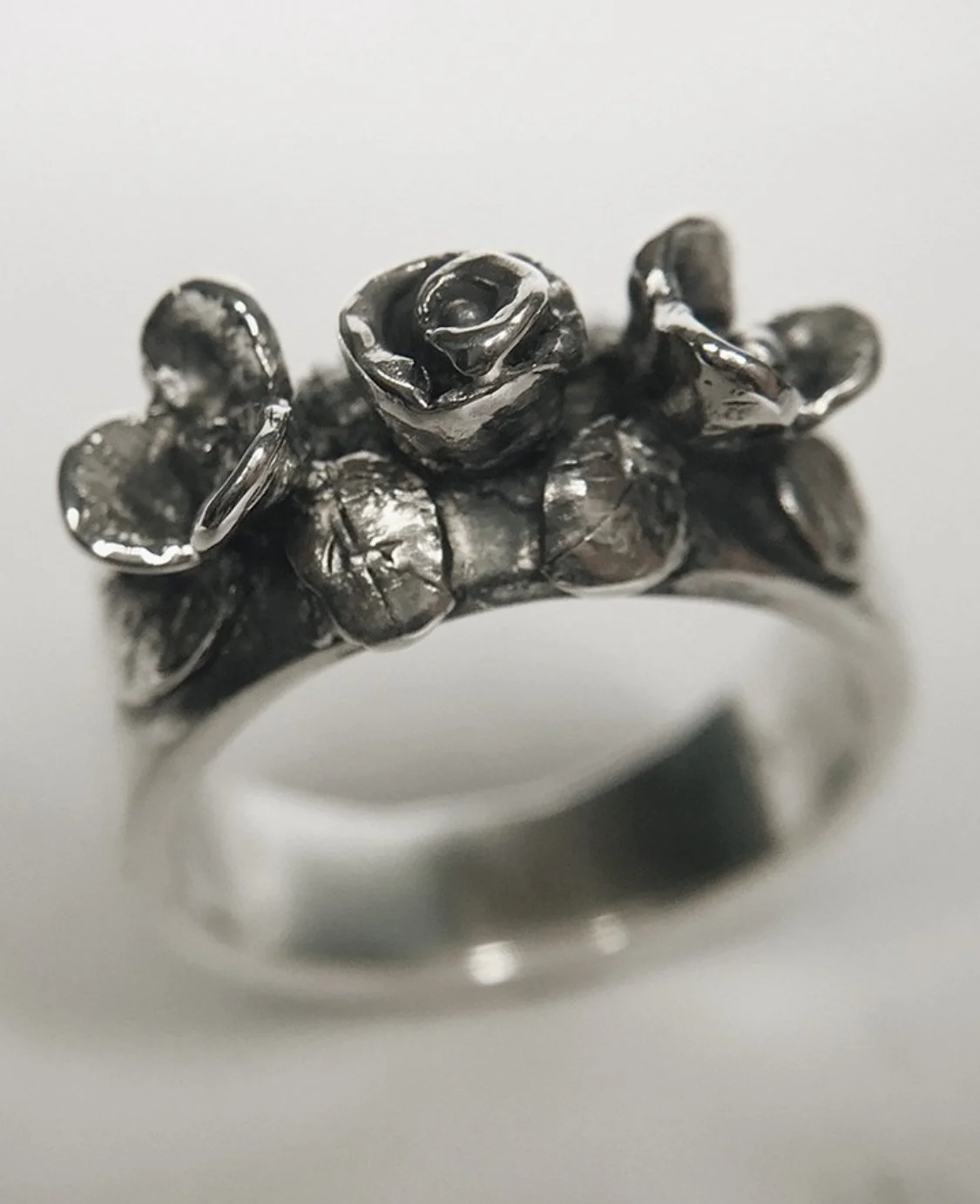 Anillo de plata con diseño de rosas pequeñas y hojas, en estilo escultórico