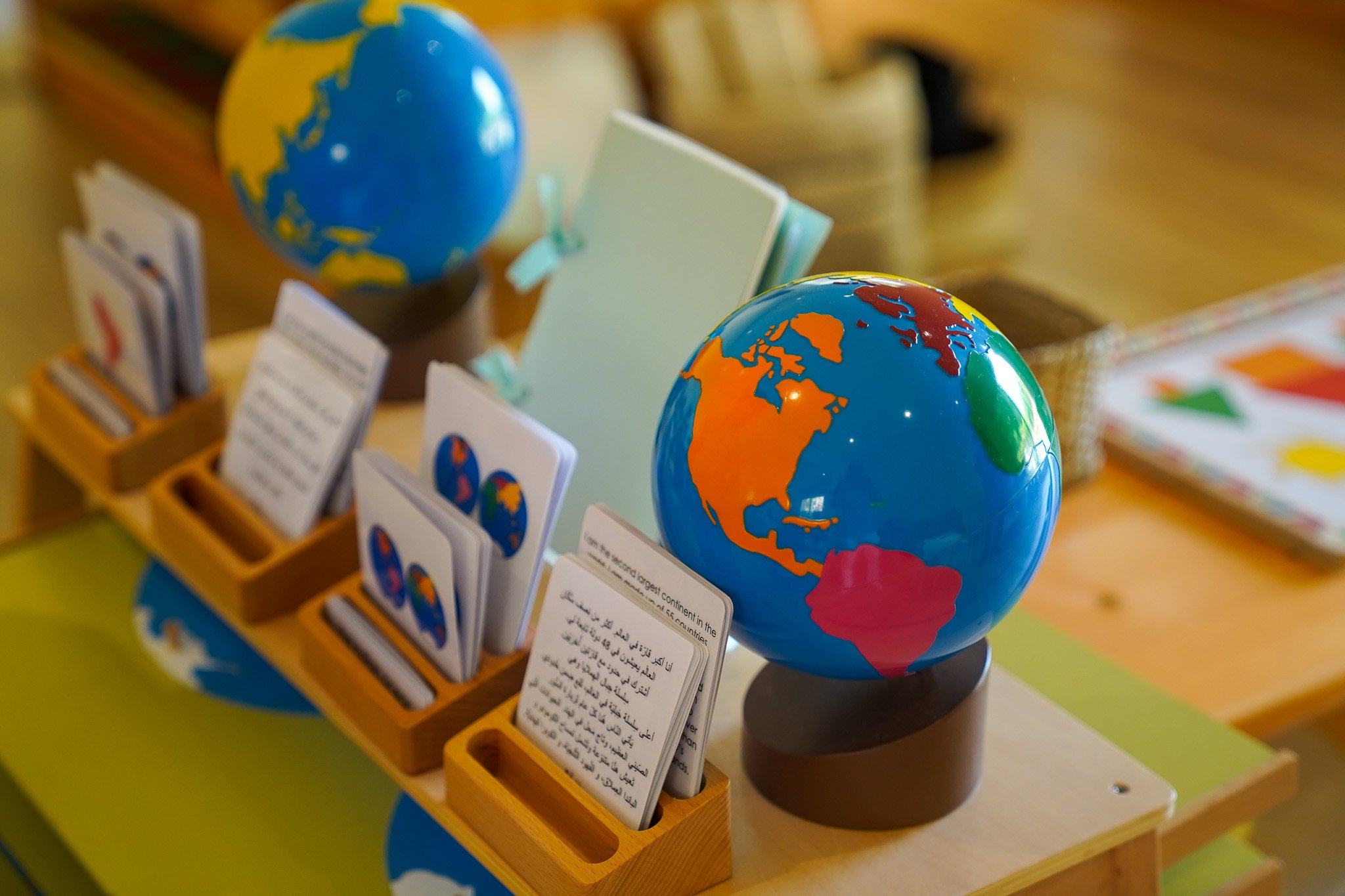 كرويتان صغيرتان، إحداهما تُظهر أمريكا الشمالية والجنوبية، والأخرى تُظهر في الغالب أوروبا وأفريقيا، موضوعة على حوامل خشبية على مكتب. كما توجد عدة بطاقات تعليمية مغلفة بصور ونصوص، بعضها بلغات متعددة، مرتبة في حاملات خشبية قريبة.