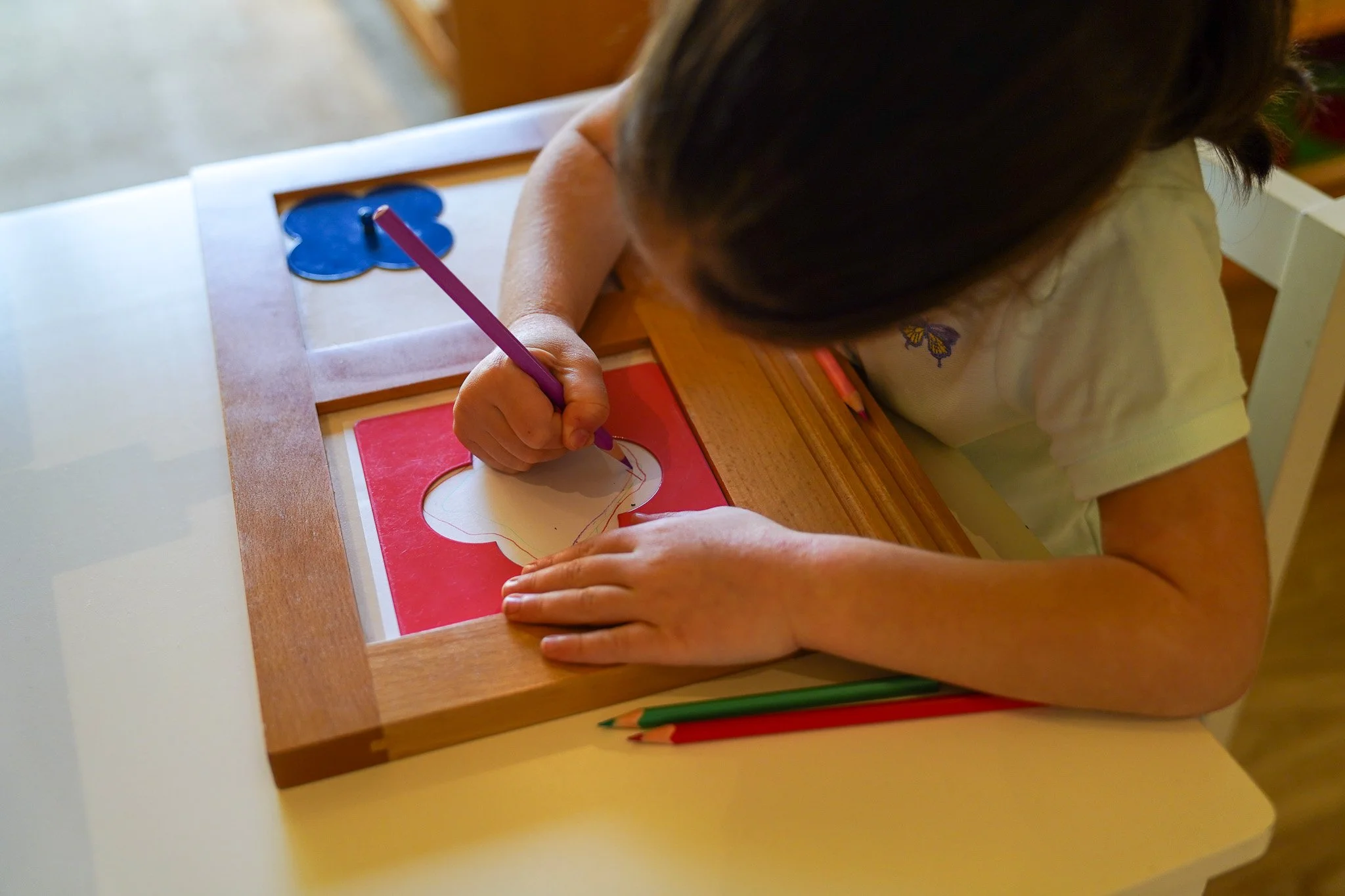 طفلة ترسم على ورقة بأقلام رصاص ملونة وتركز على مشروعها الفني على طاولة.