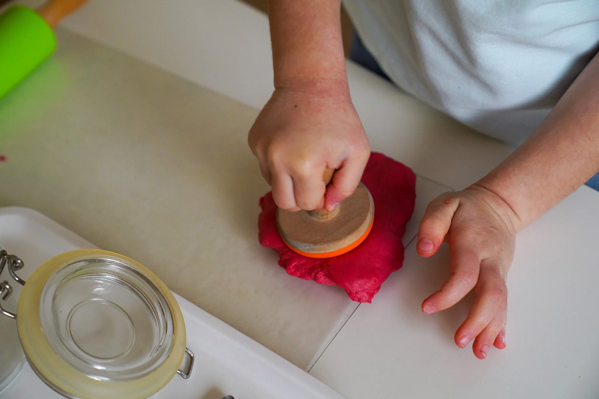 يد طفل تضغط على ختم على سطح العجين الأحمر أو الطين على طاولة المطبخ.