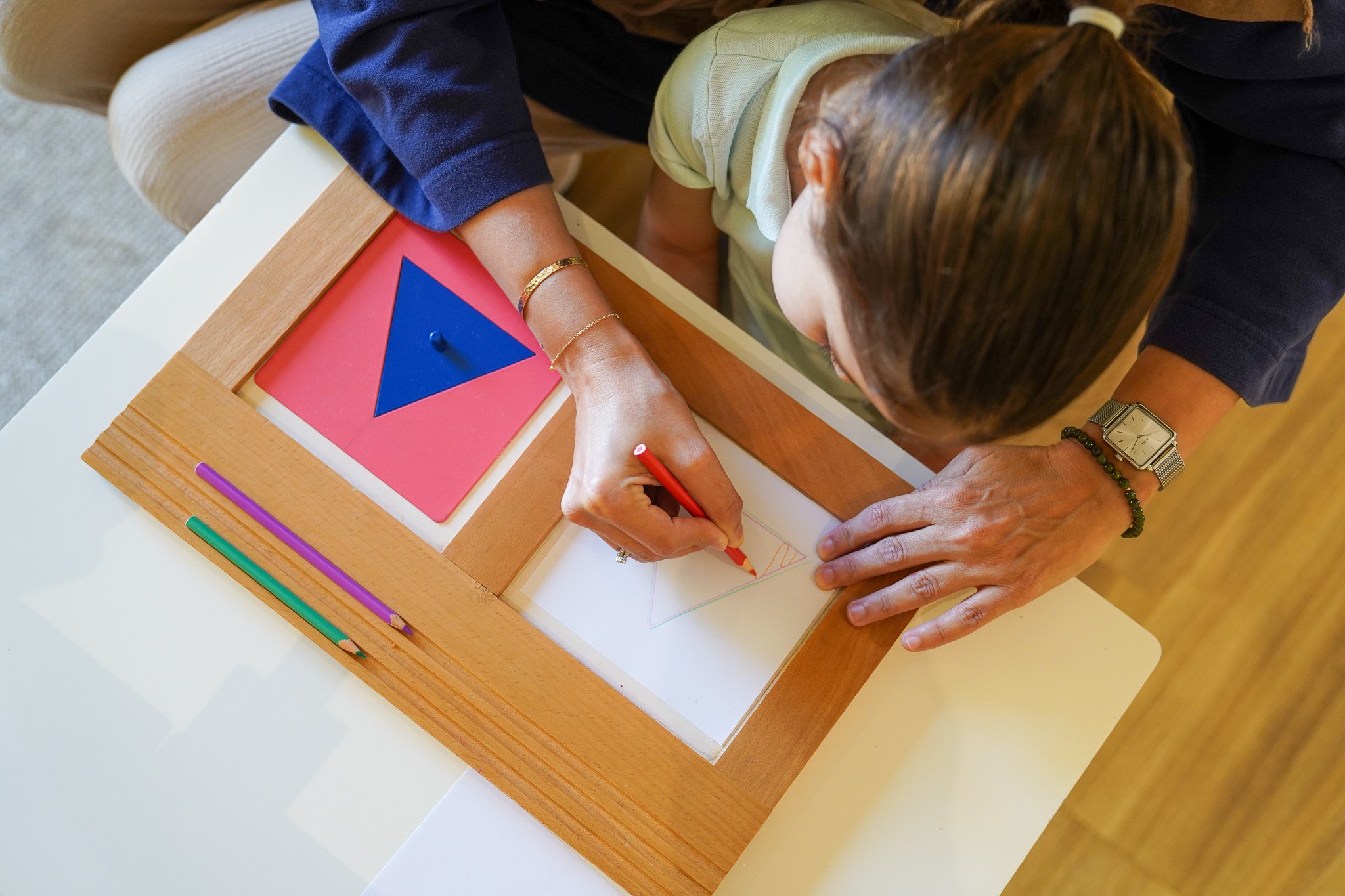 شخص بالغ وطفل يقومان برسم مثلث هندسي على مكتب مع أحجية هندسية.
