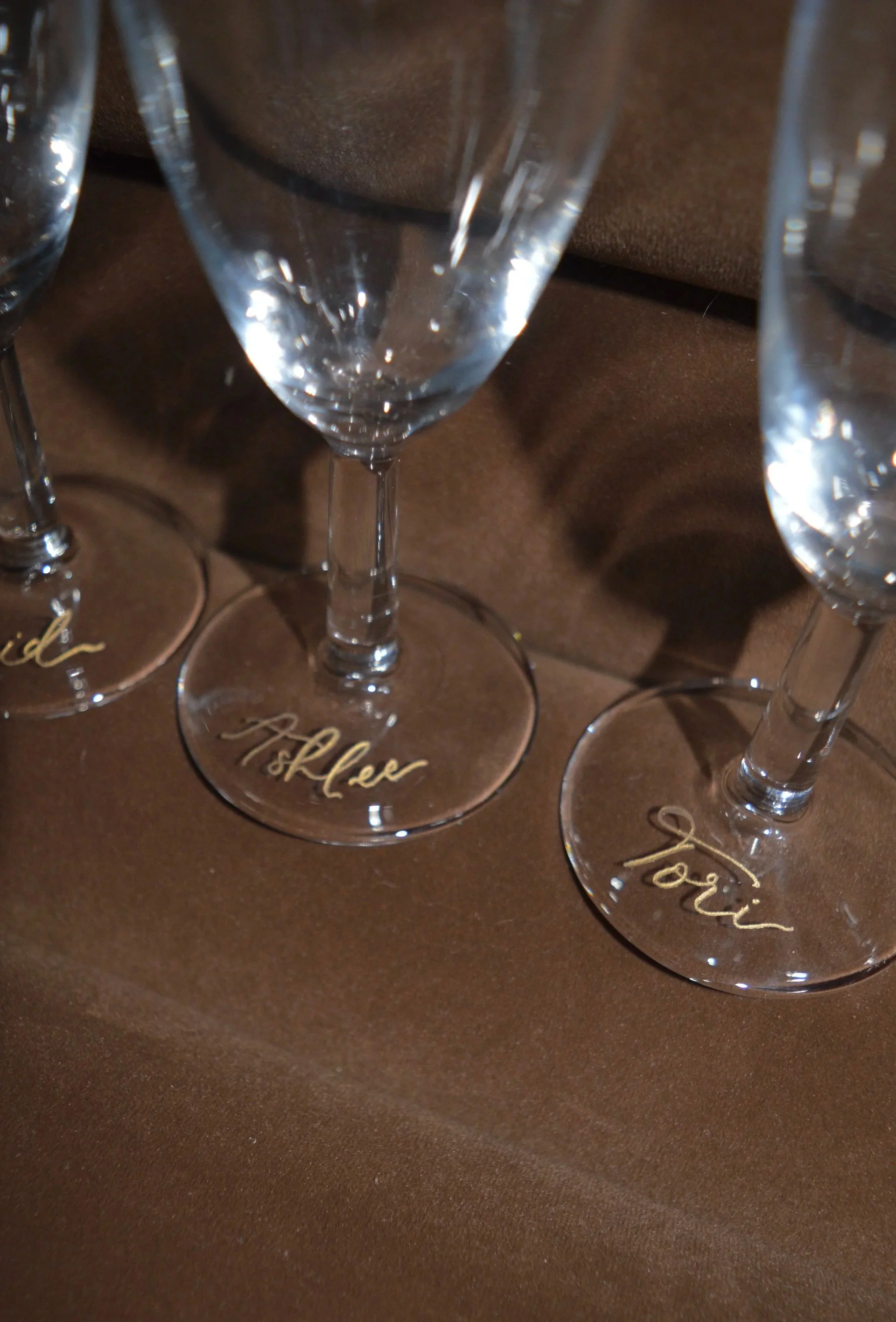 Three champagne flutes with gold script on the base, placed on a brown surface.