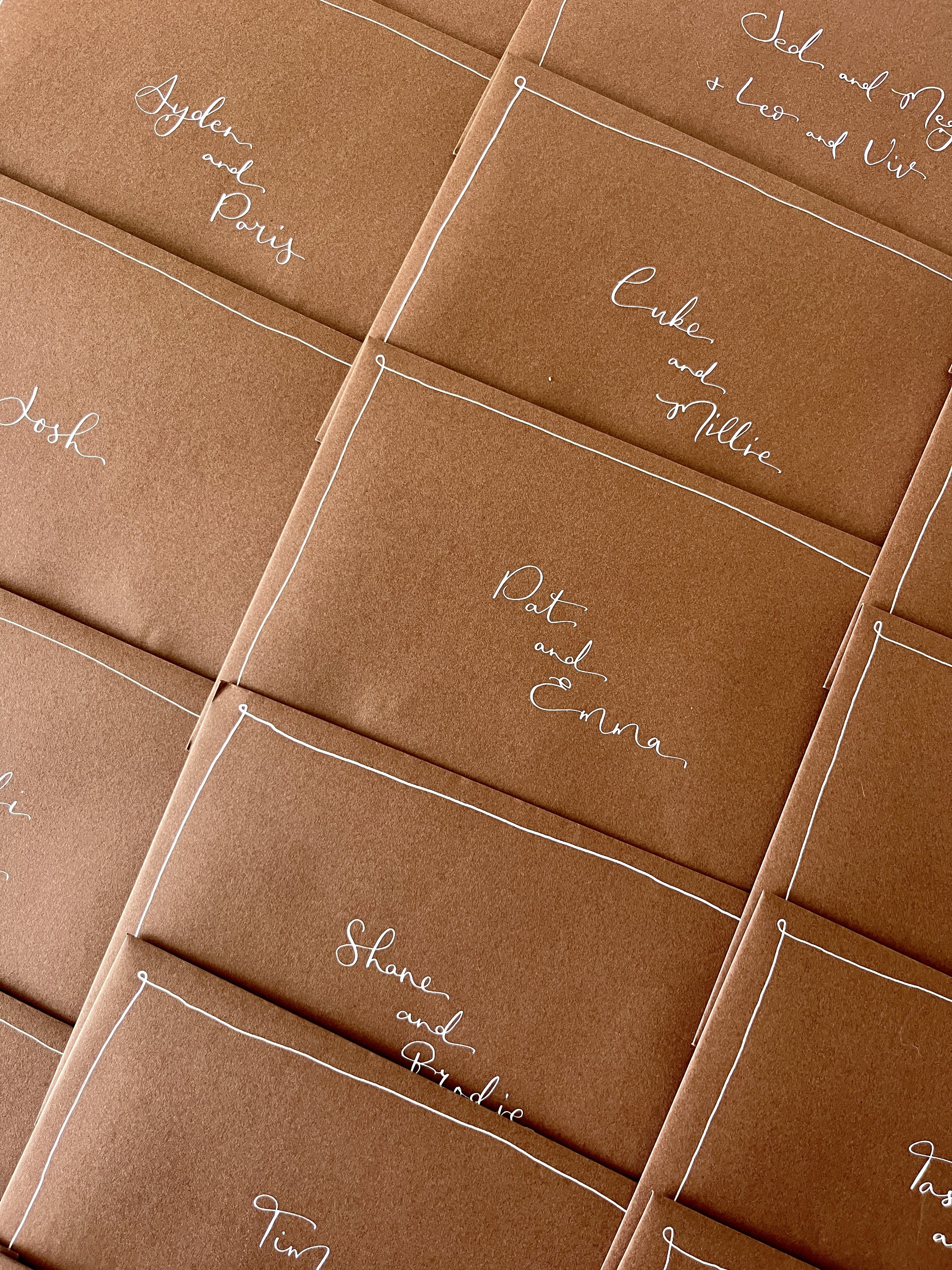 Brown envelopes addressed with white cursive calligraphy handwritten names on each, arranged in a grid pattern.