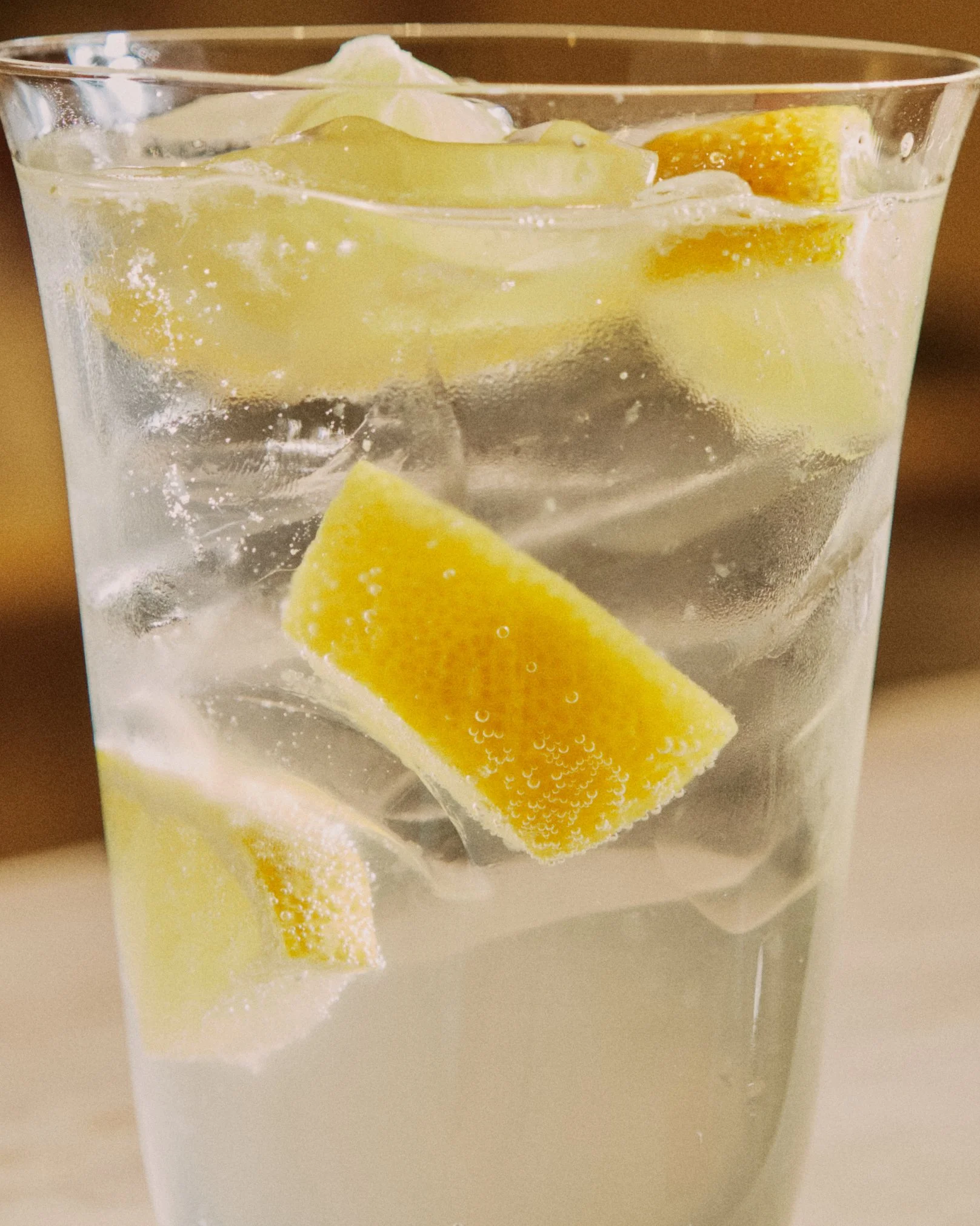 A glass of sparkling water with ice cubes and lemon wedges.