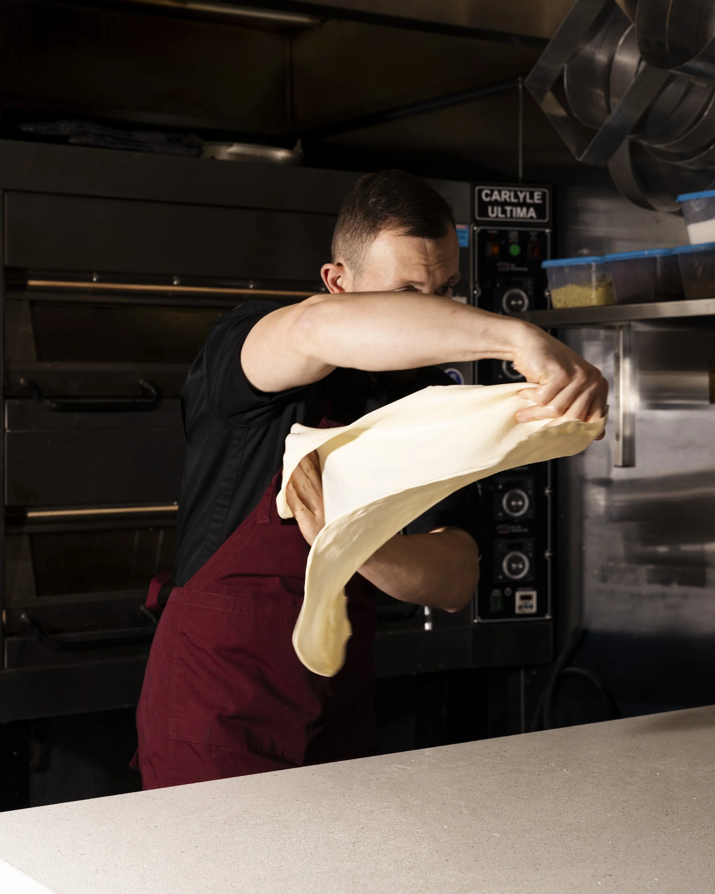 A person in a kitchen preparing food, with a homemade filo, behind a counter. Rated best greek pastry in Melbourne