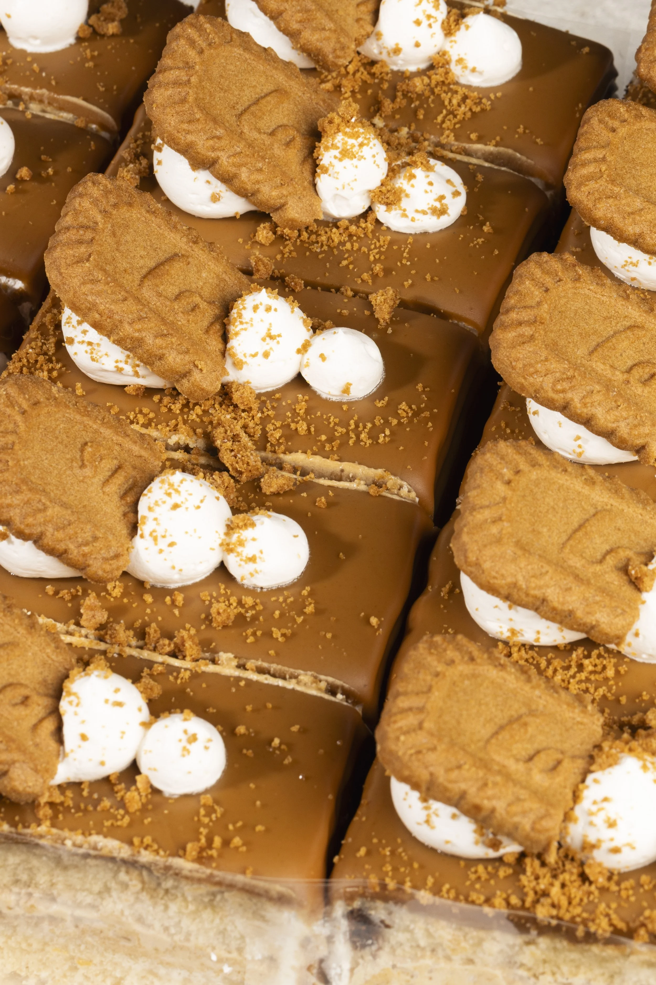 Close-up of chocolate caramel bars topped with whipped cream, cookie halves, and crushed cookie crumbs.