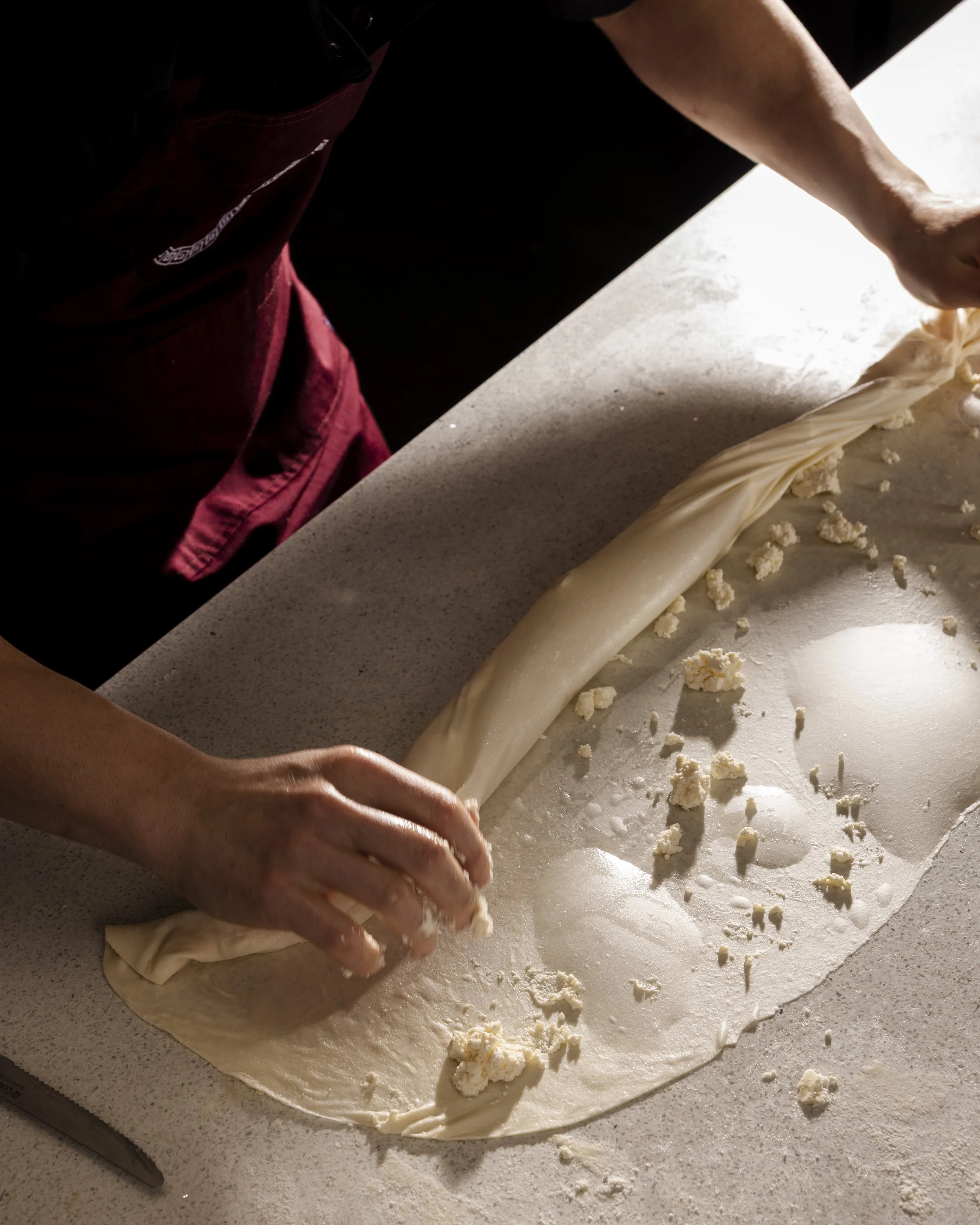 Person preparing dough with cheese on a kitchen counter, cutting the dough into small pieces.