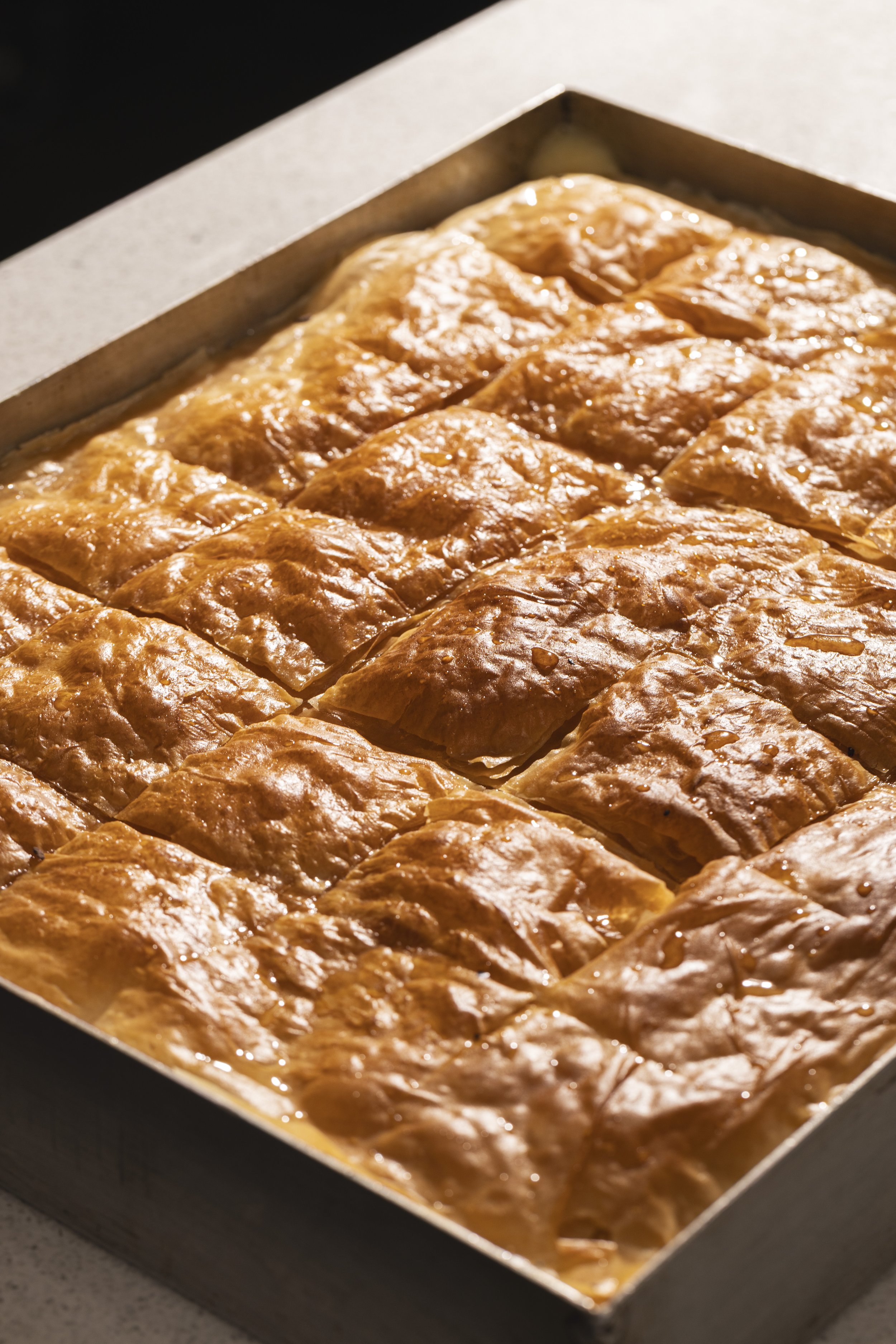 Close-up of baklava dessert arranged in layers on a baking tray, glazed with syrup.