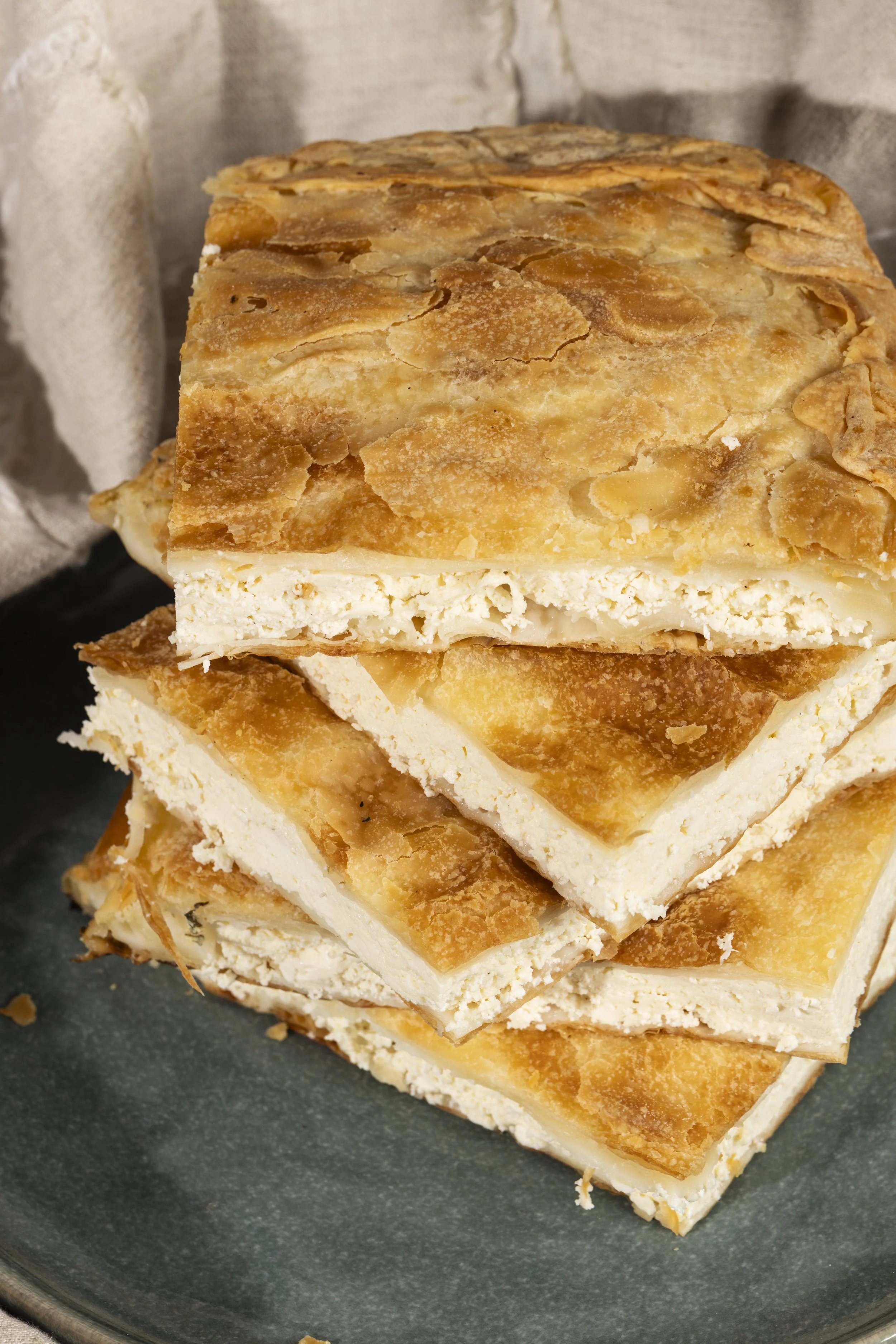 Stack of layered pastry bars with a flaky, golden-brown crust and a white filling, on a dark gray plate.