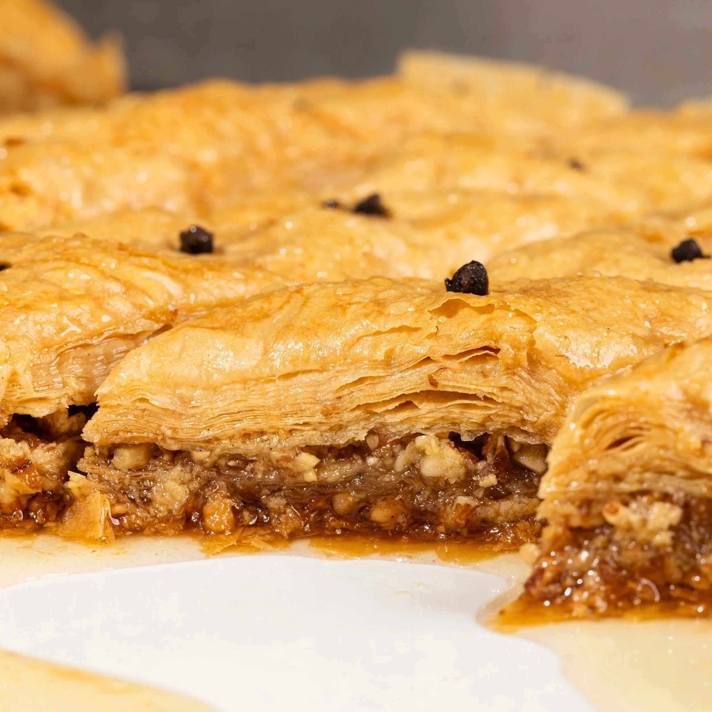 Close-up of layered apple pie with a flaky golden crust, with a filling of apples, cinnamon, and black peppercorns visible underneath.