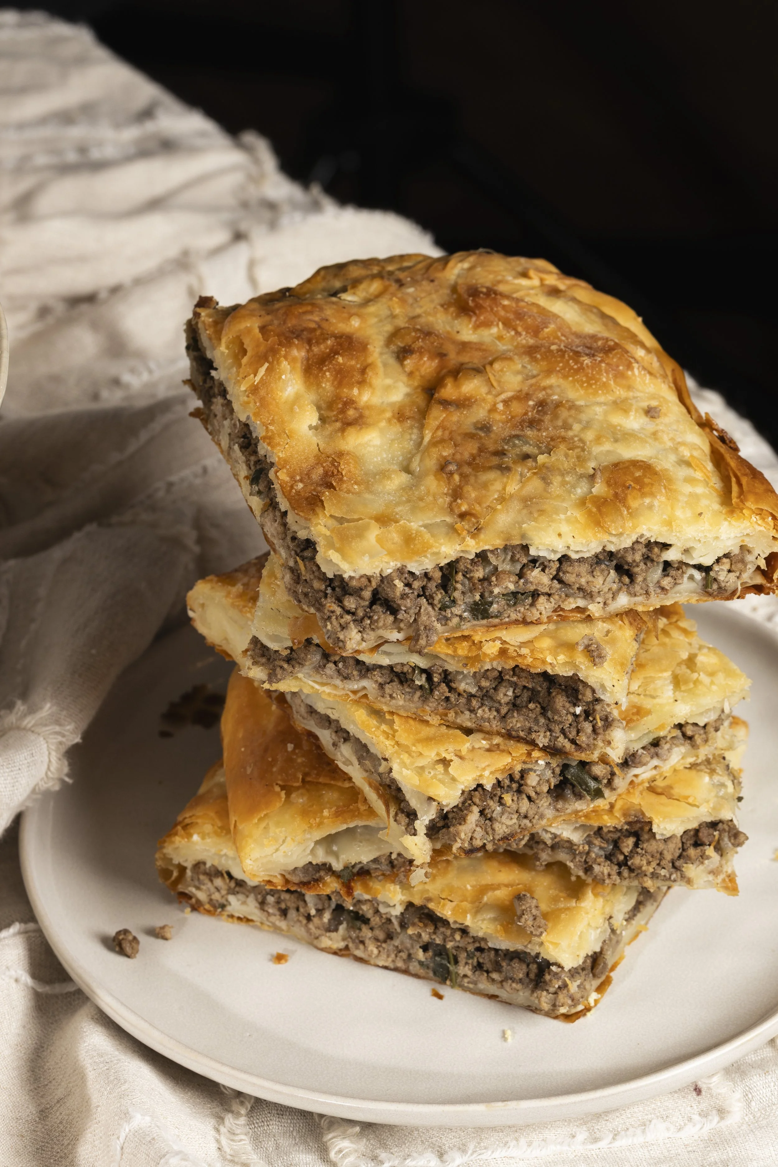 A slice of homemade meat pie with a golden, flaky crust and seasoned ground beef filling, placed on a white plate.