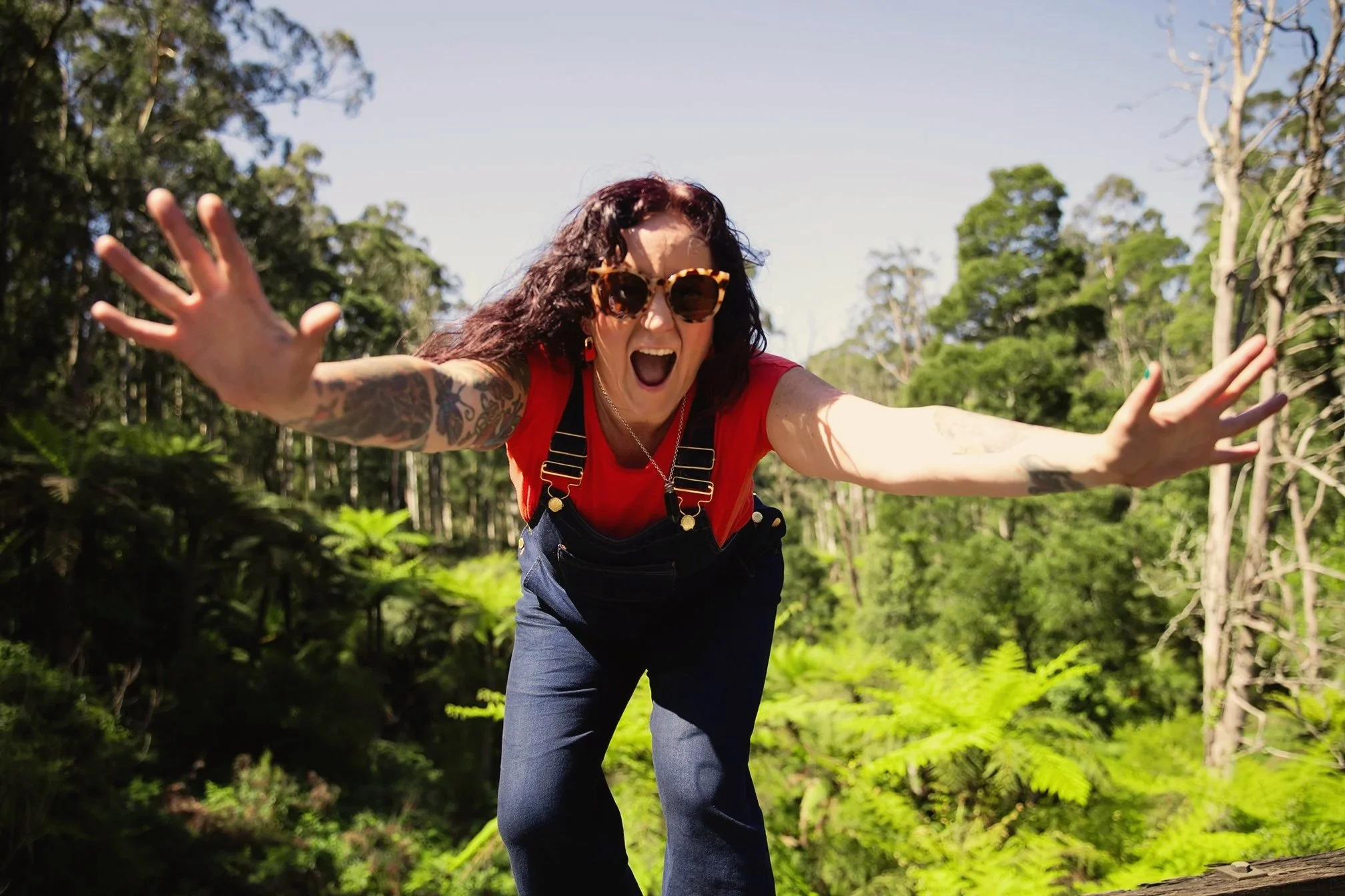 Woman reaches toward the camera with arms outstretched in a lush green landscape