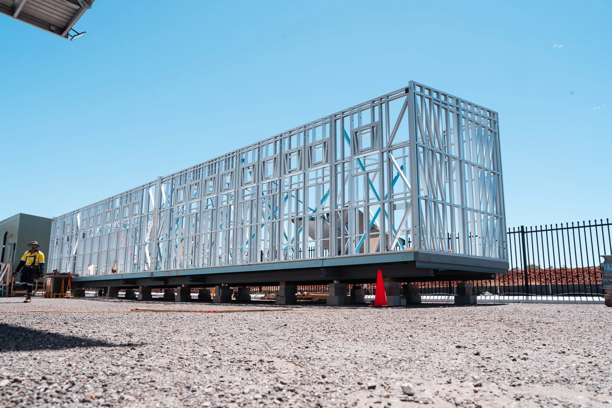 Construction site with a building frame on stilts, partially assembled with a clear blue sky above.