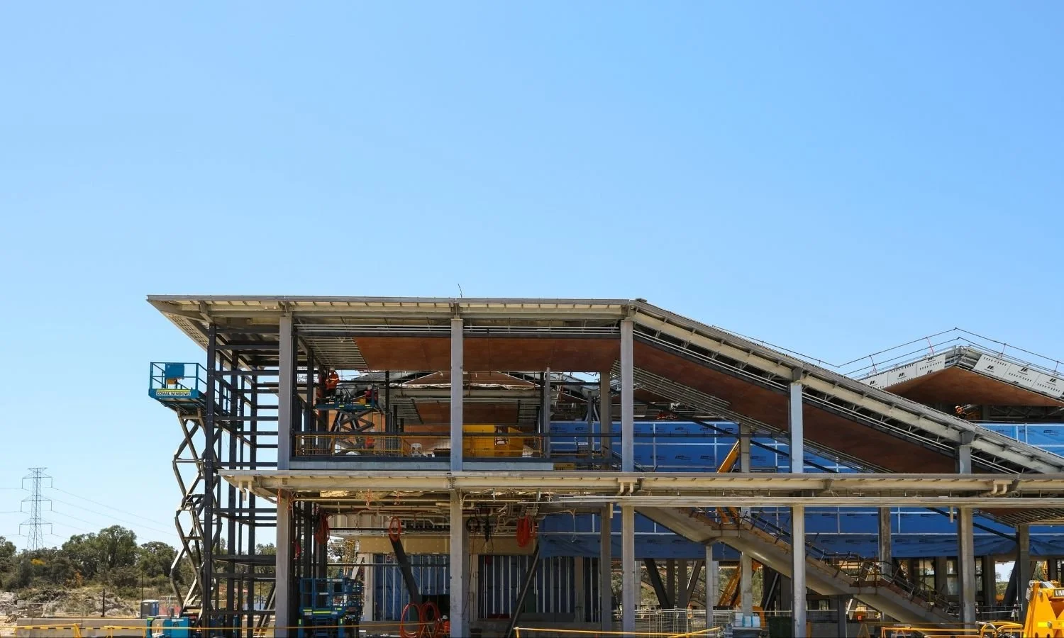 Construction site of a multilevel building with steel framework and scaffolding against a clear blue sky.