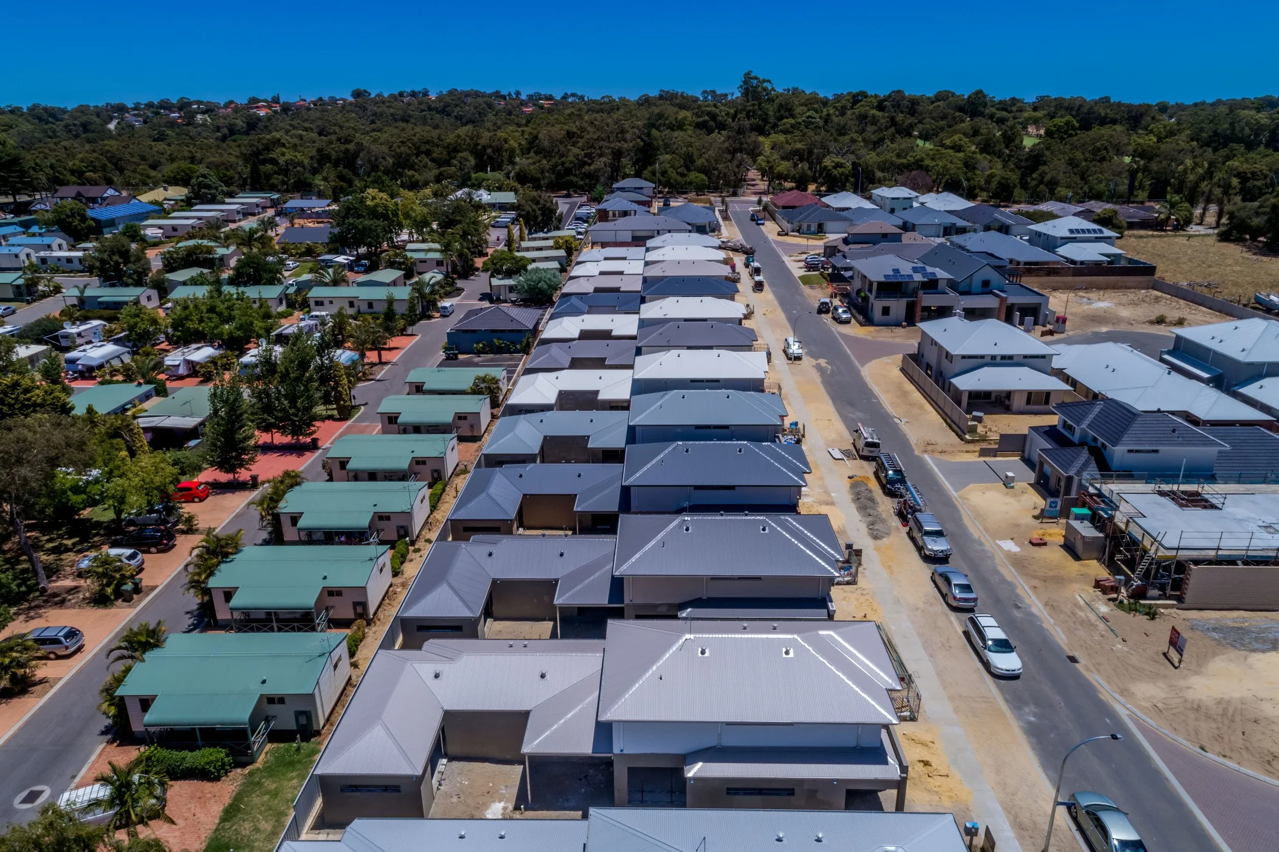 Aerial view of a suburban neighborhood with newly built houses, some under construction, surrounded by trees and greenery.