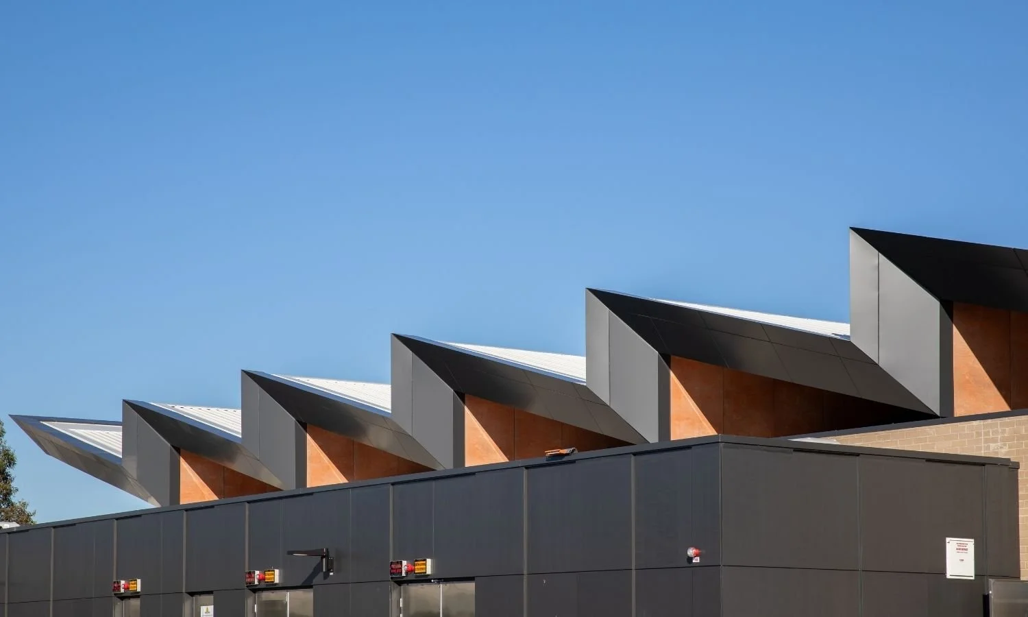 Modern building with multiple angular roofs against a clear blue sky.