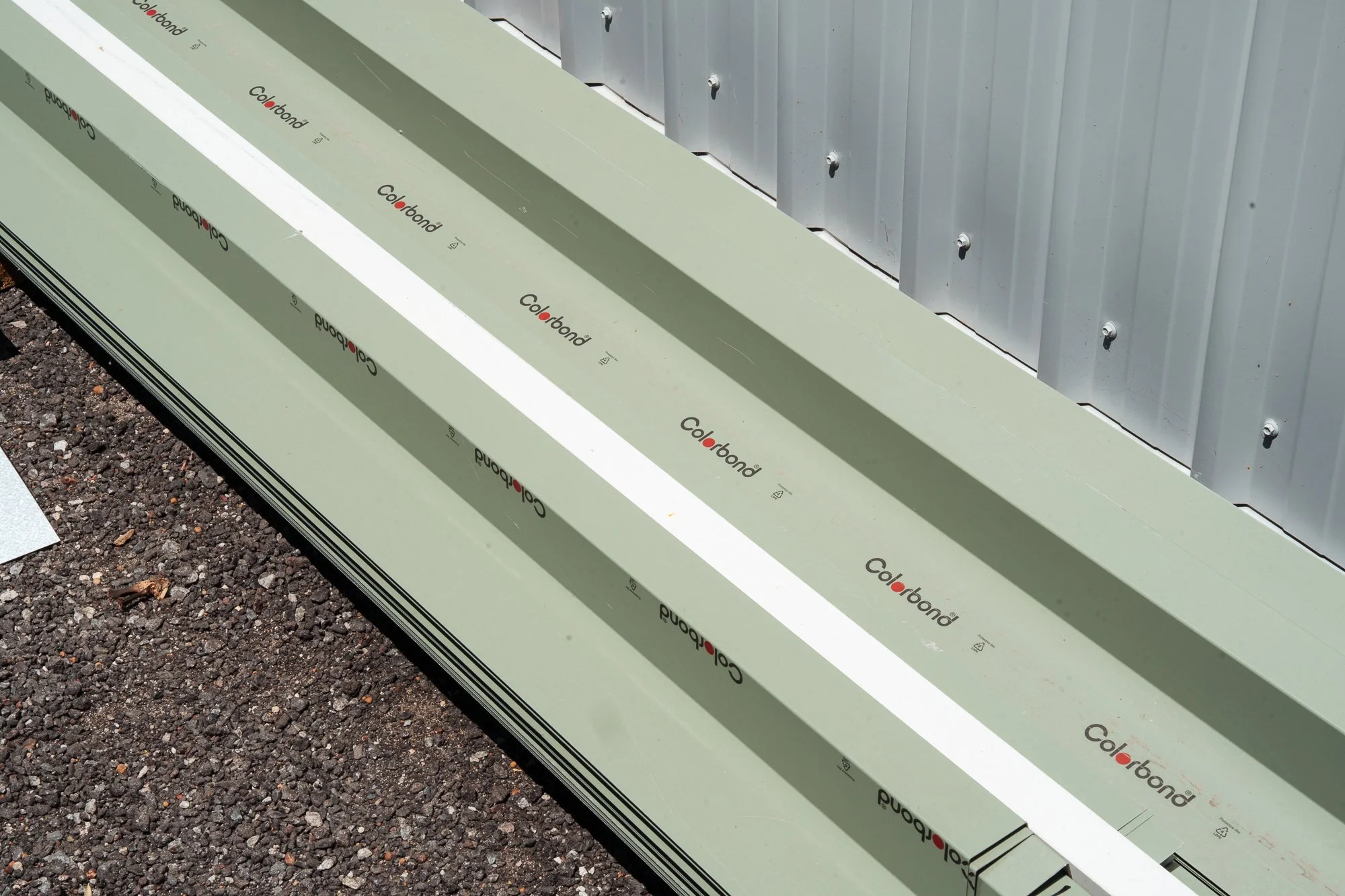 Close-up of a section of a metal building exterior with a protective green Coverbond material laid on the ground in front. The ground is gravel.