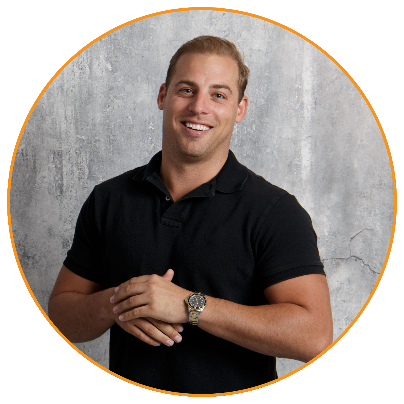 A smiling young man with short light brown hair, wearing a black polo shirt, with a gold wristwatch, standing against a gray concrete wall.