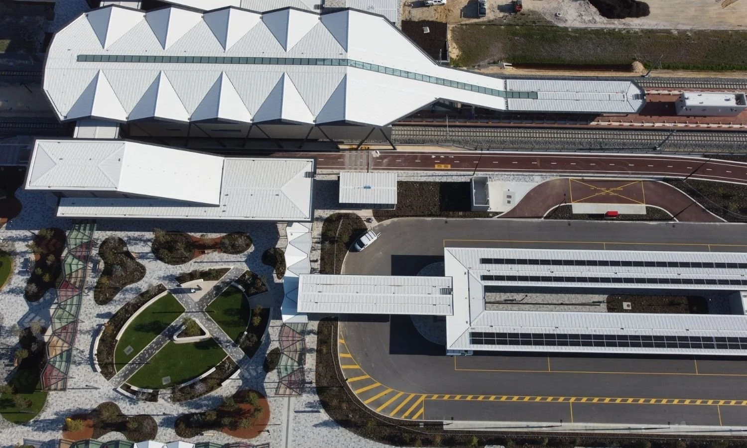 Aerial view of a modern transportation station with train tracks, platforms, and surrounding landscaped area with pathways and greenery.
