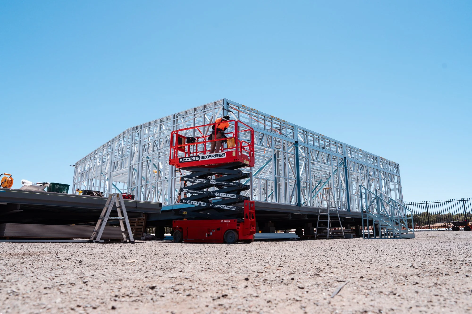 Construction worker on a mobile lift working on a steel framework of a building against a clear blue sky.