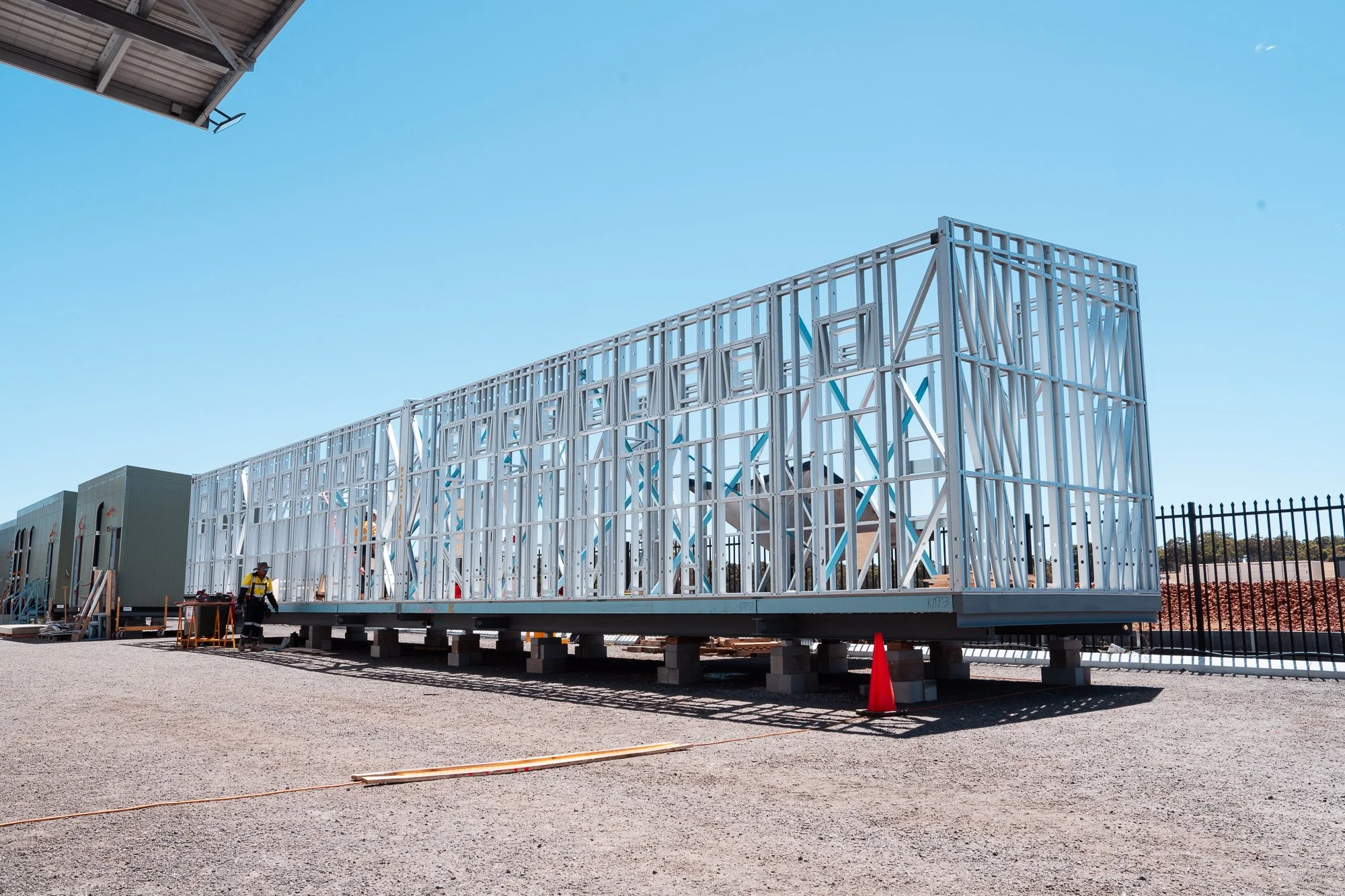 Steel framework structure on a construction site, with workers nearby and a blue sky overhead.