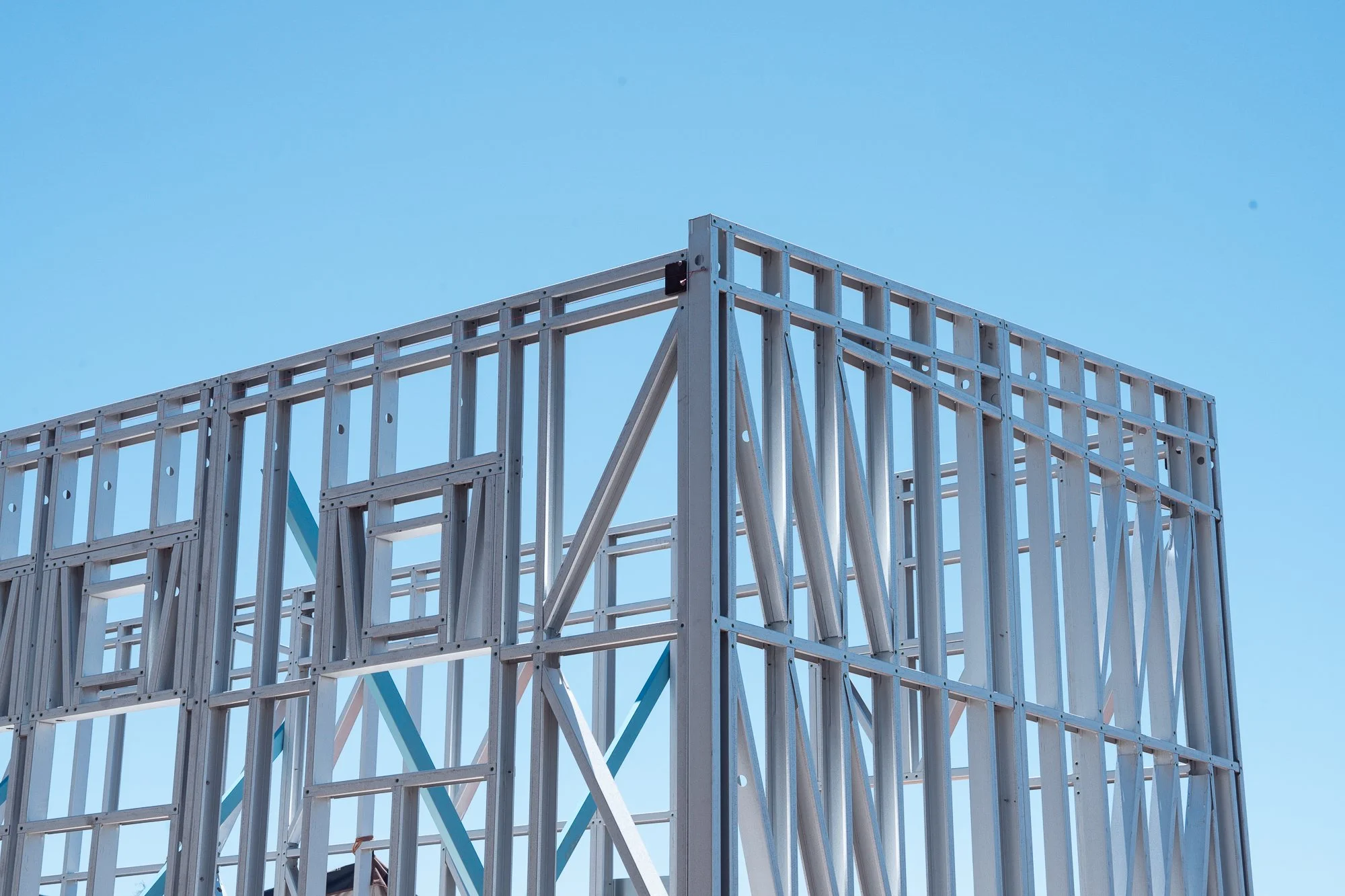 Frame of a building under construction made of metal beams against a clear blue sky.