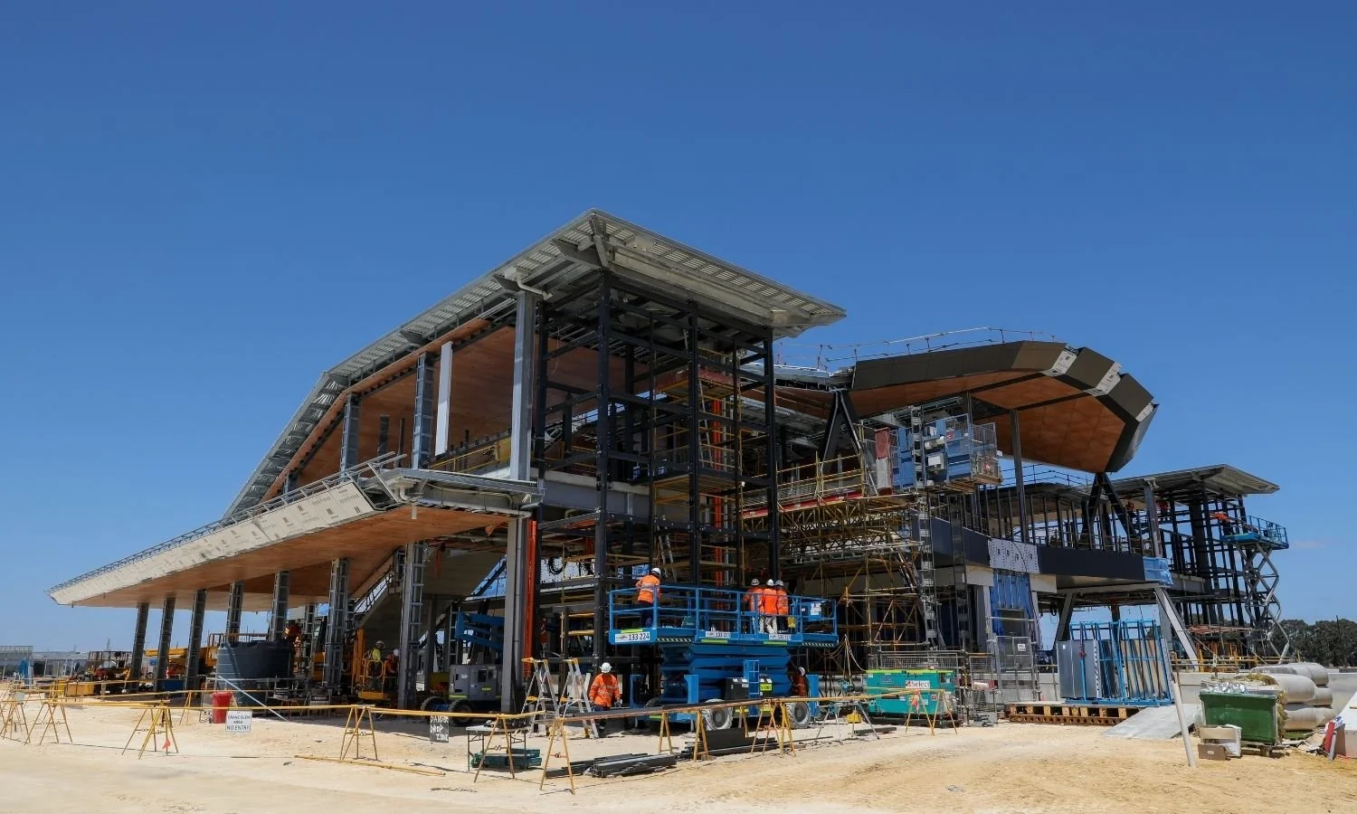 Under construction building with steel framework, scaffolding, and construction workers, set against a clear blue sky.