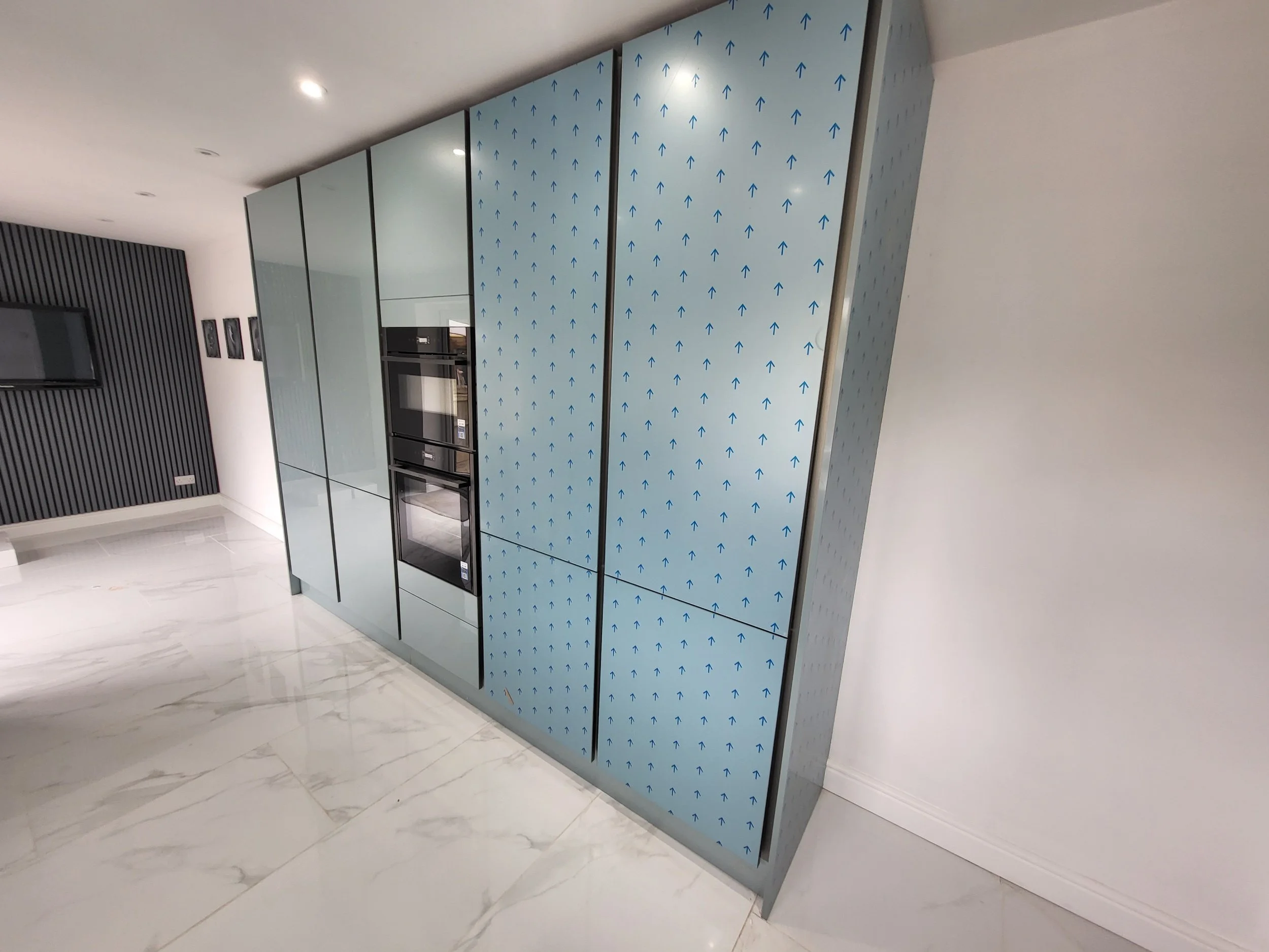 Modern kitchen area with a built-in oven, blue patterned cabinets, white marble floor, and a black striped accent wall.