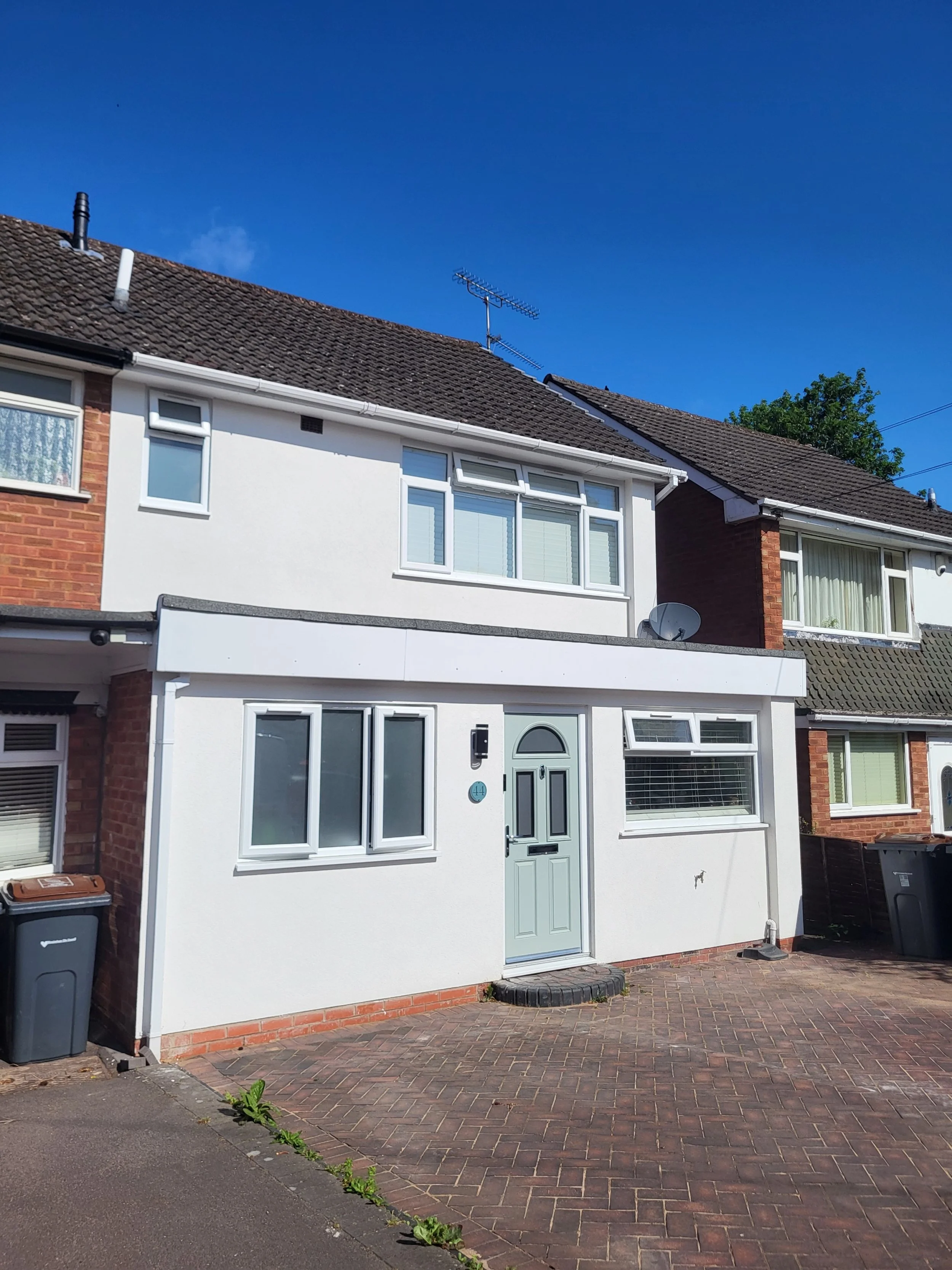 Front exterior view of a modern, white, two-story house with a gray front door, large windows, and a paved driveway under a clear blue sky.