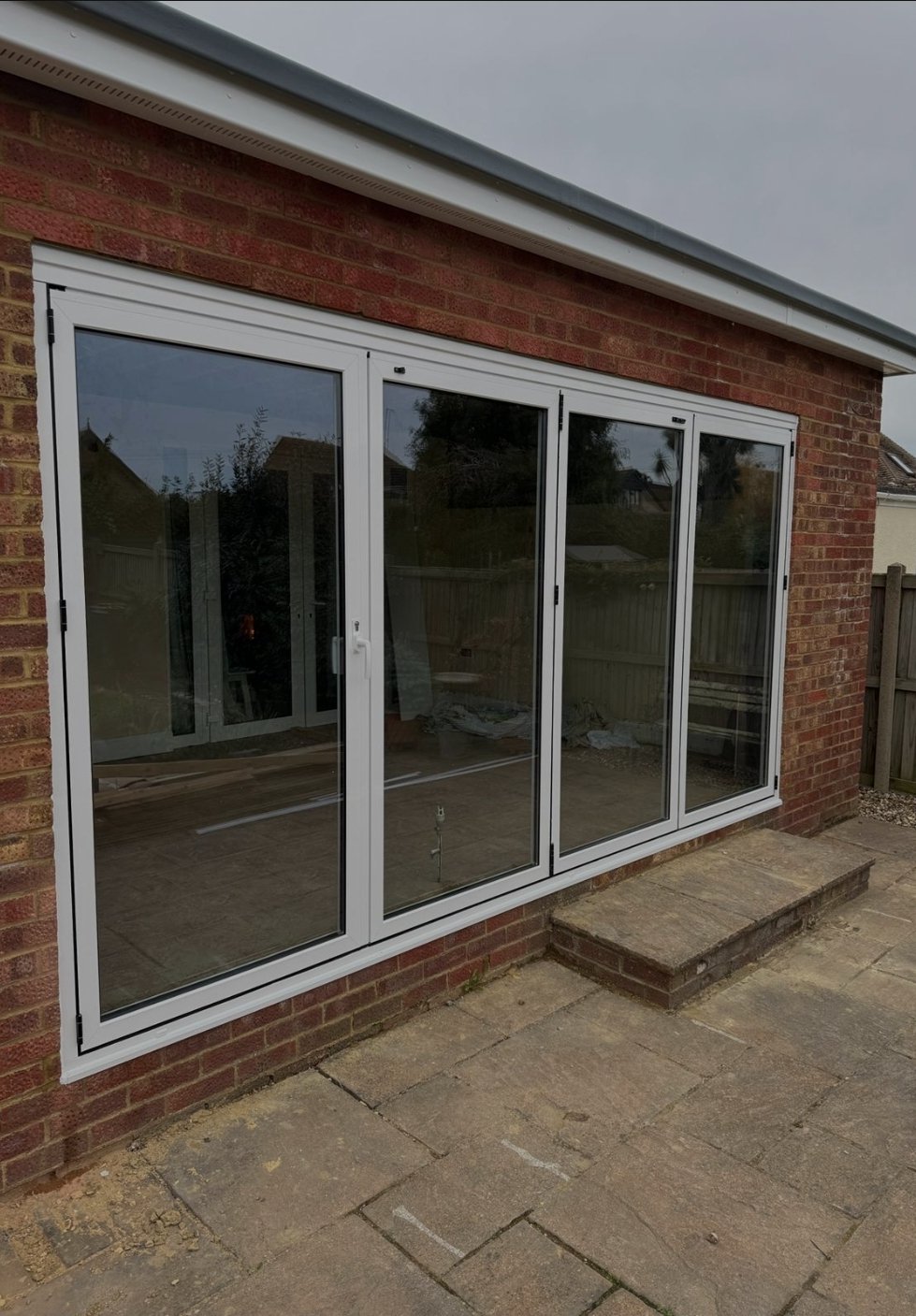A sliding glass door installed on a brick wall, with a small stone step outside on a paved area.
