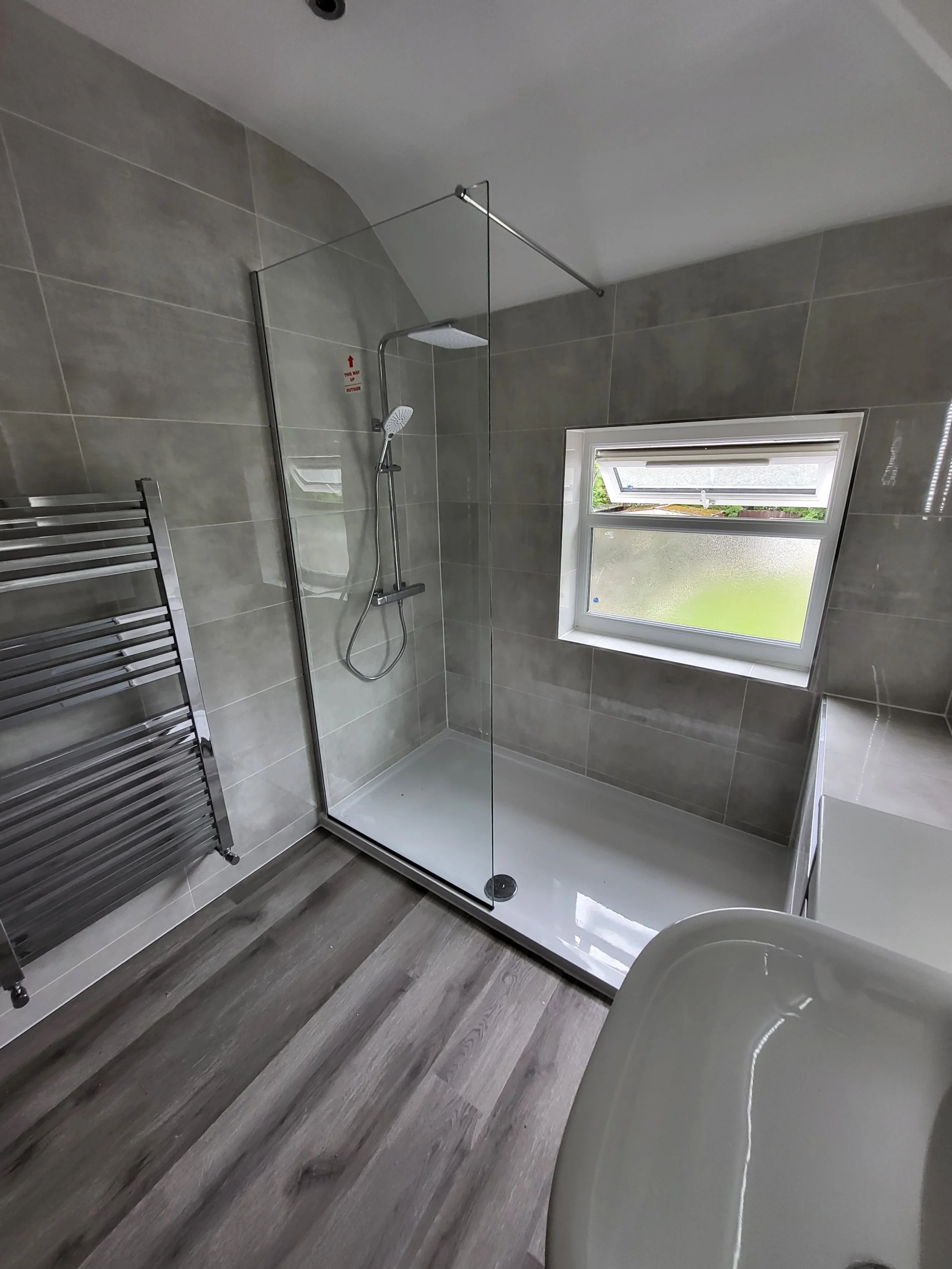 Modern bathroom with a walk-in shower, frosted window, and wood-look flooring.