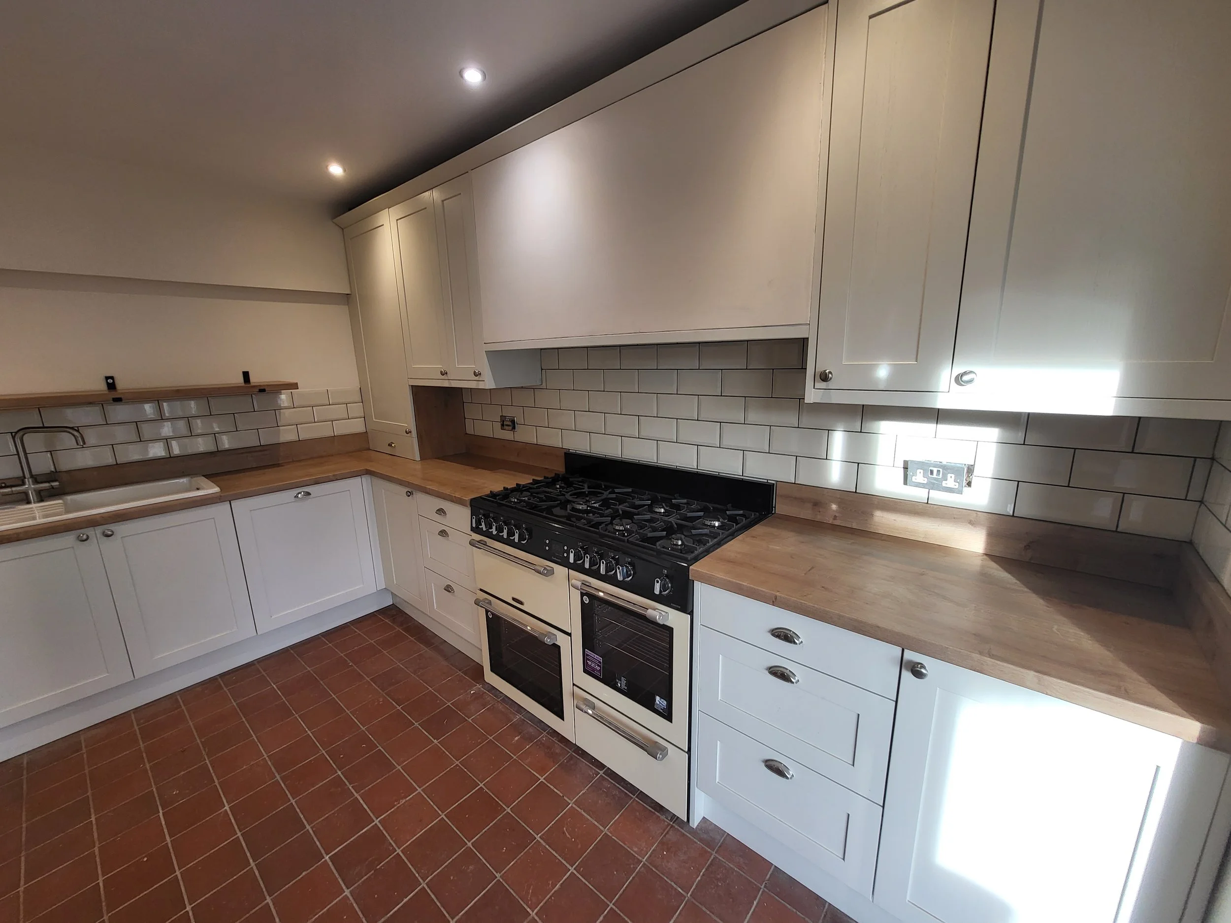 Modern kitchen with white cabinets, wooden countertops, a gas stove with two ovens, a tiled backsplash, and brick-patterned floor tiles.