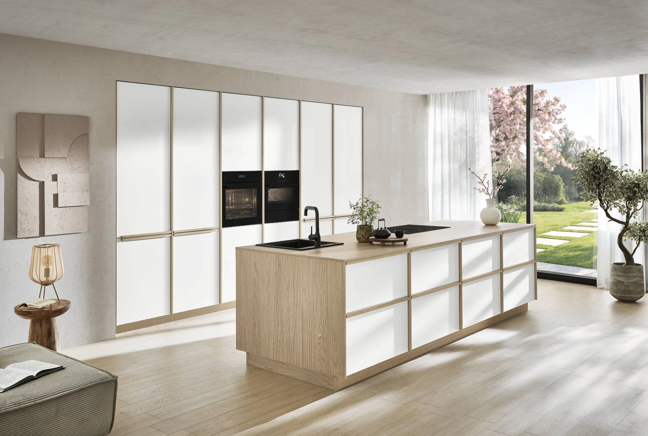 Moderne, helle Kücheninsel mit Holz und weißen Flächen, mit Blick auf einen großen Garten mit Kirschblütenbaum durch große Fenster
