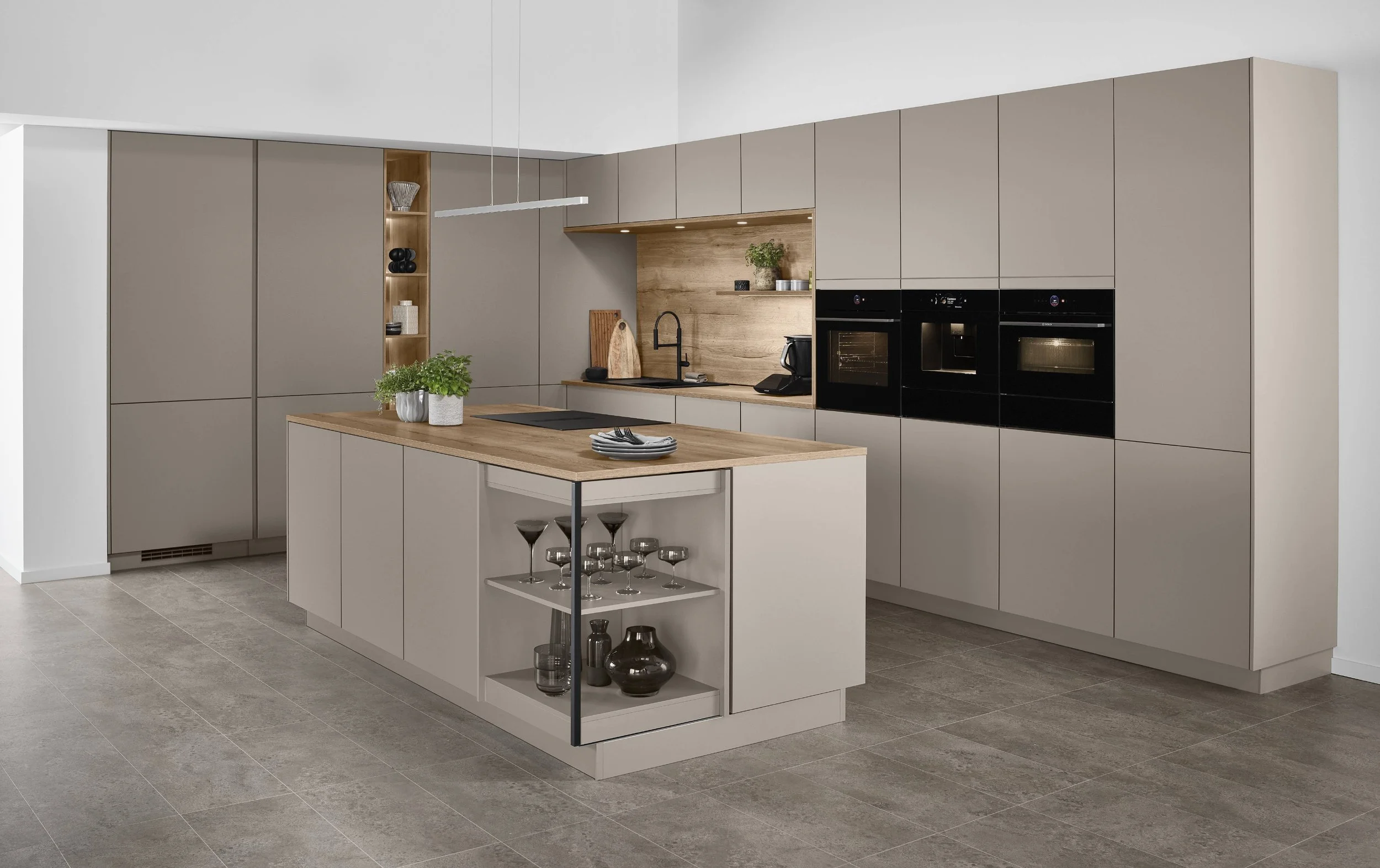 Moderne offene Küche mit beige Schränken, Holzarbeitsflächen und -rückwand, Kochinsel mit Geschirr, integrierte Backöfen, Geschirr, Pflanzen und Küchenutensilien.