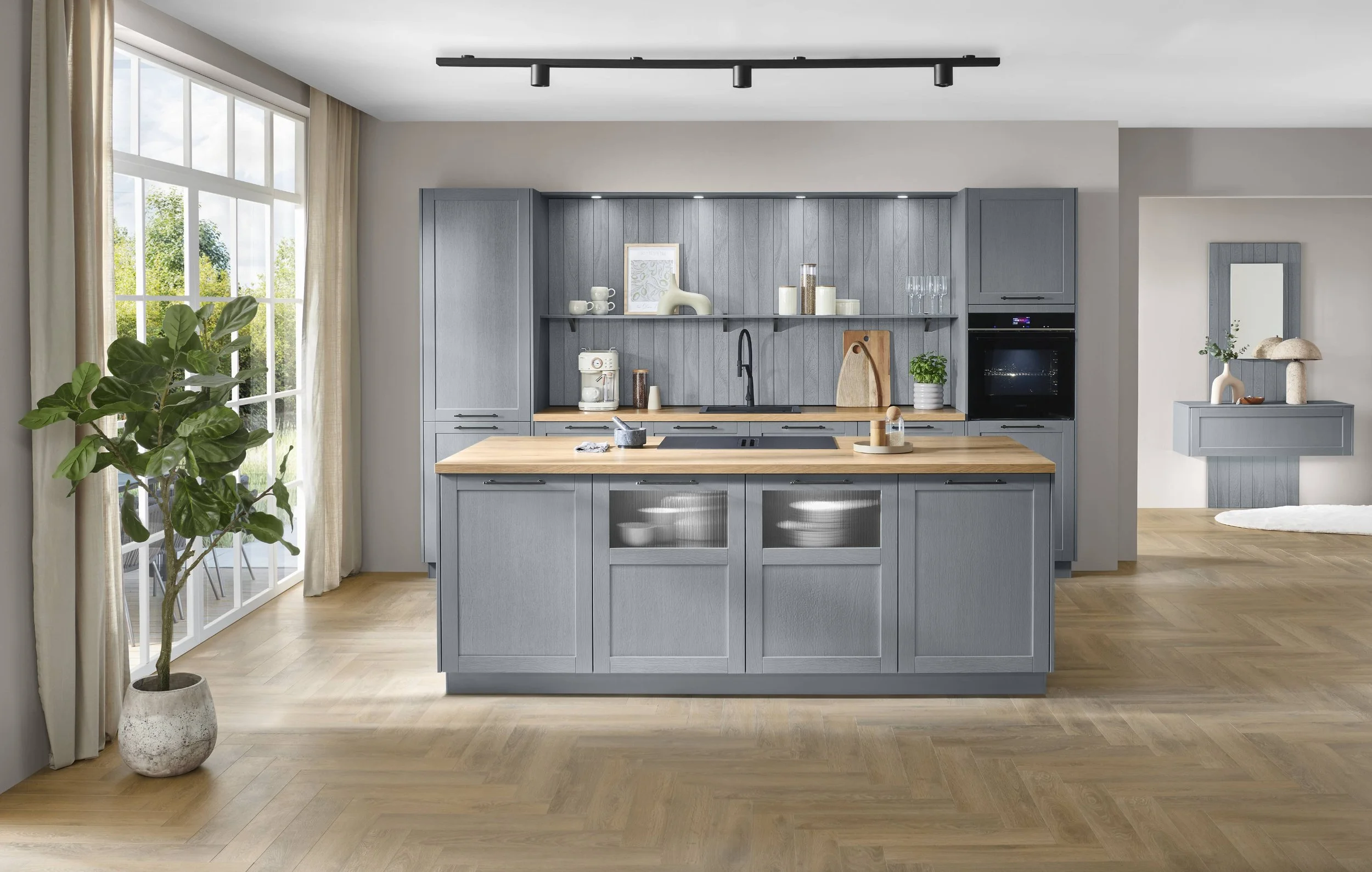 Moderne helle Küche mit grauen Holzschränken, Kücheninsel mit Holztisch, große Fenster mit weißen Vorhängen, Holzboden, Dekorationen auf offenen Regalen, Pflanzen, Backofen und Kaffeemaschine.